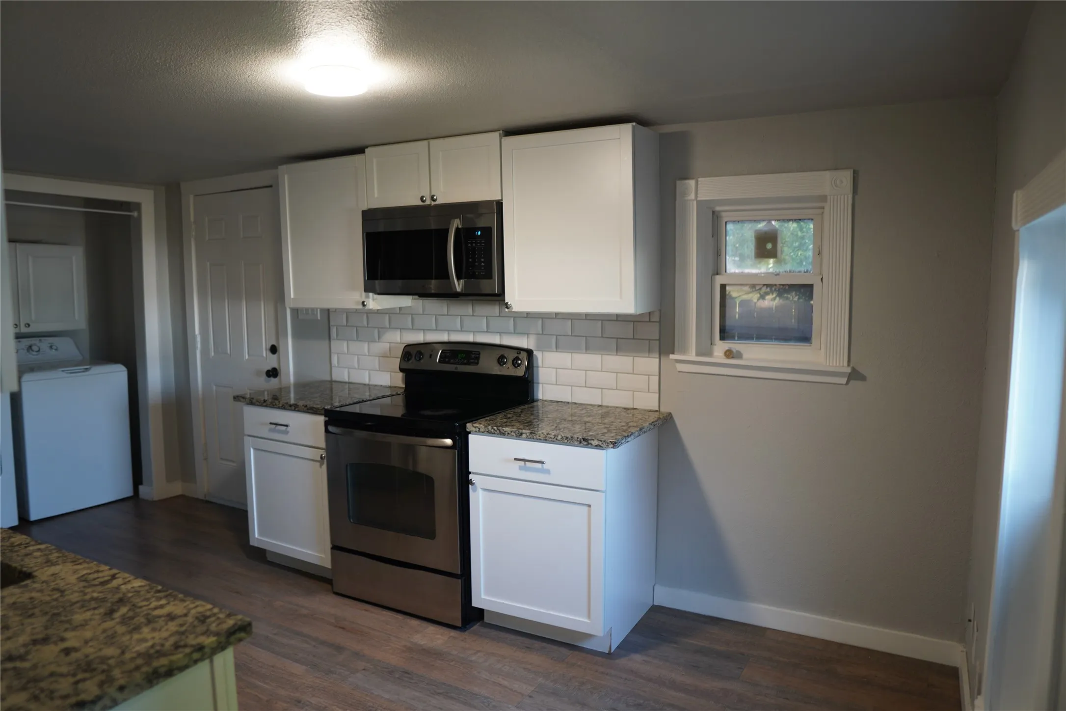 Modern kitchen featuring white cabinetry, granite countertops, stainless steel appliances, a subway tile backsplash, and wood-finish flooring