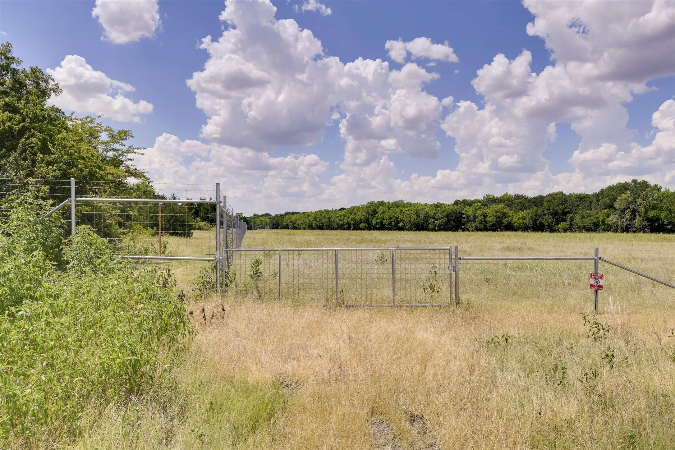 Gate to hay field with creek along treeline in distance.