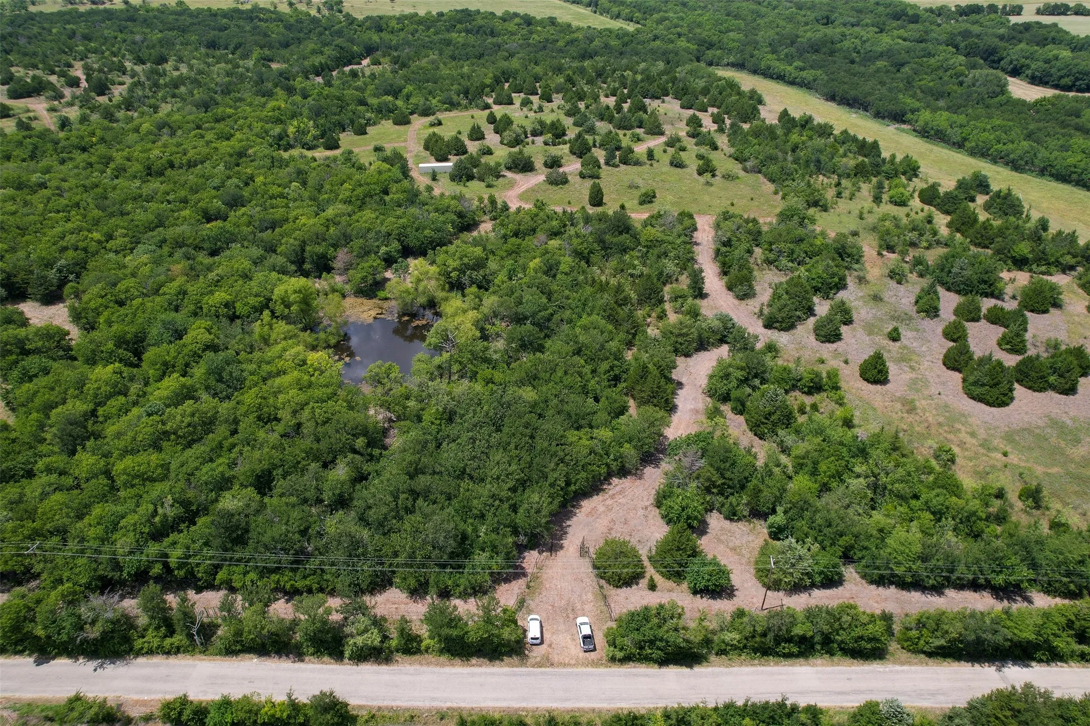 Main Gate is in front of two white cars, plenty of road frontage, cleared trail around the property.