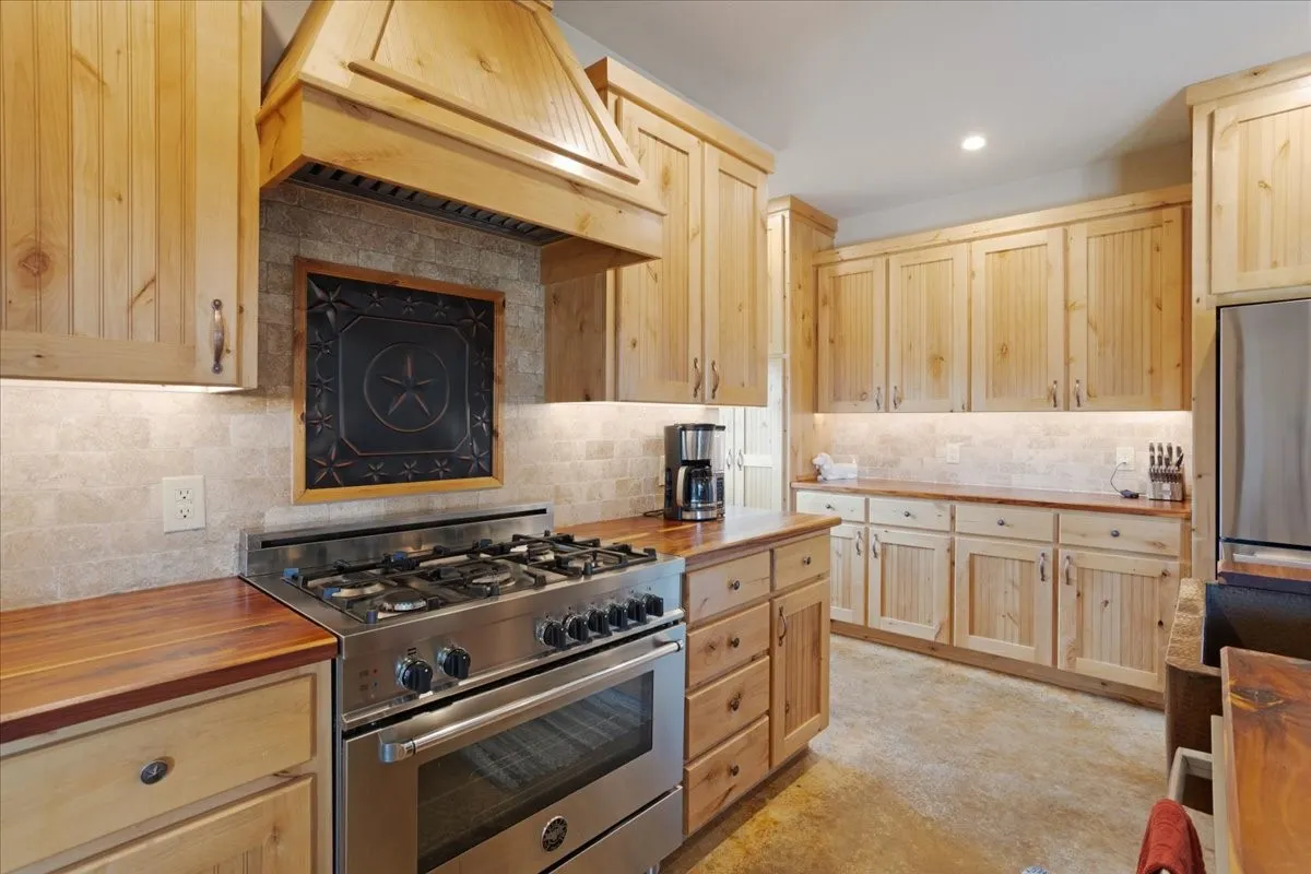 Spacious kitchen featuring natural wood cabinetry, wood-finish countertops, stainless steel range with gas burners, and a tile backsplash with under-cabinet lighting