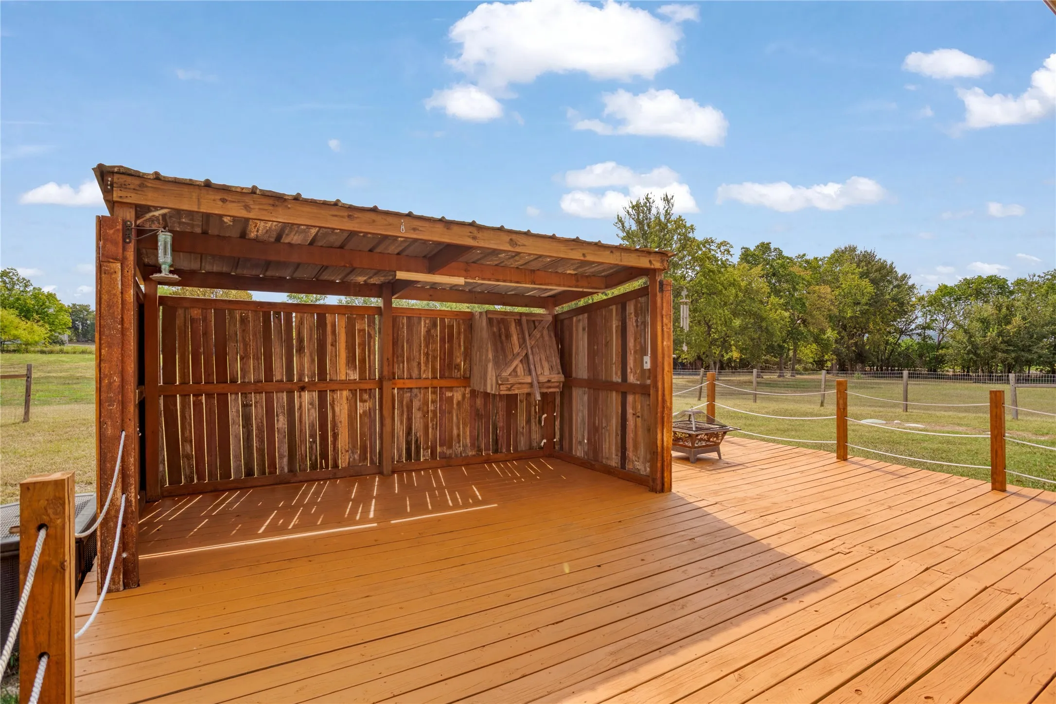 Expansive outdoor deck featuring a covered wooden structure, wood-finish flooring, and a rope railing