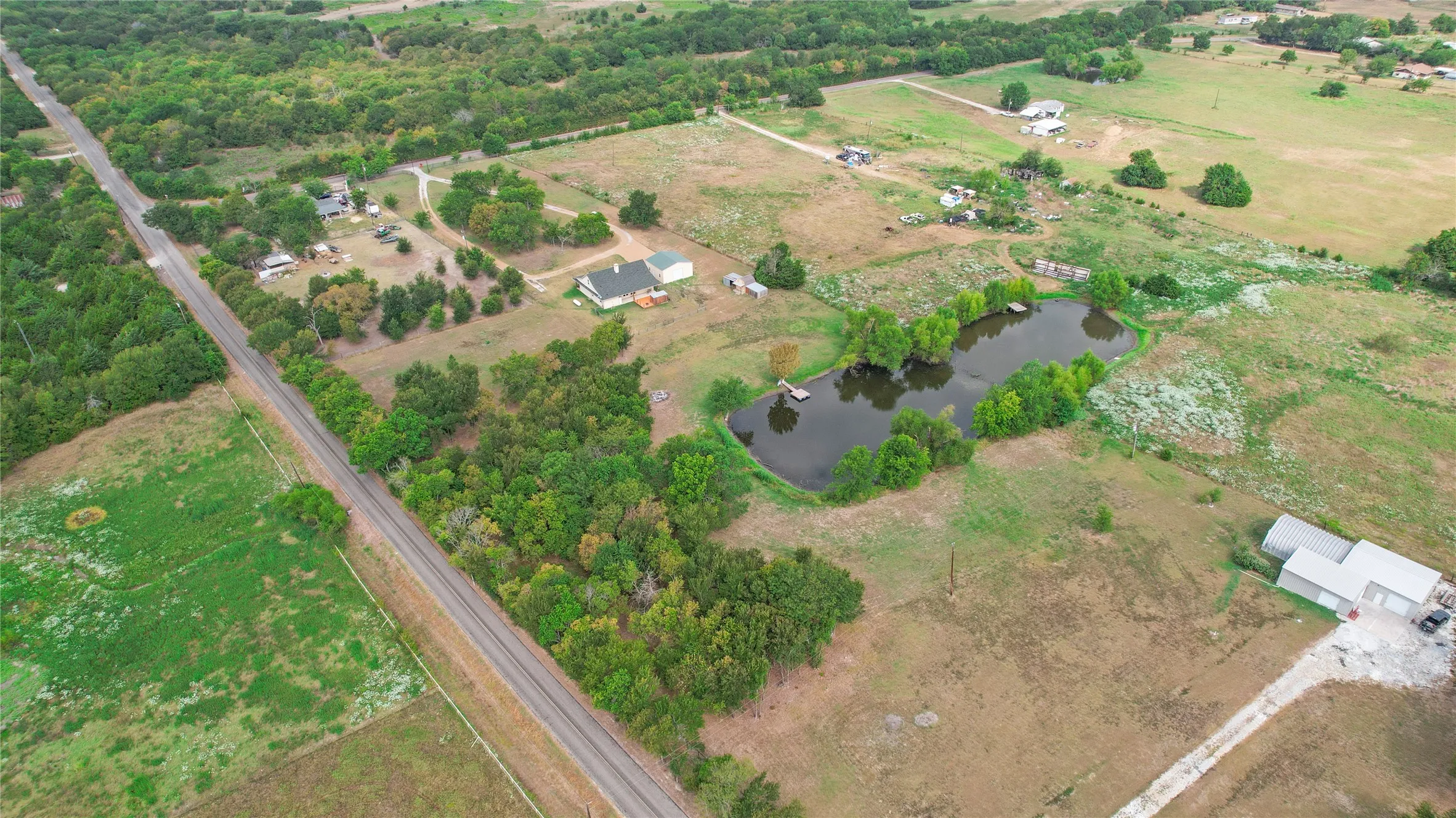 Expansive rural property featuring a prominent pond, surrounded by mature trees and open land
