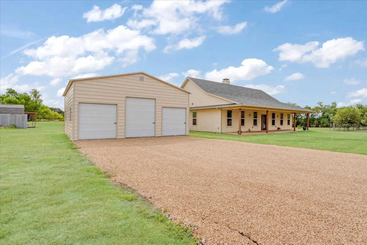 Expansive gravel driveway leading to a three-bay metal garage building