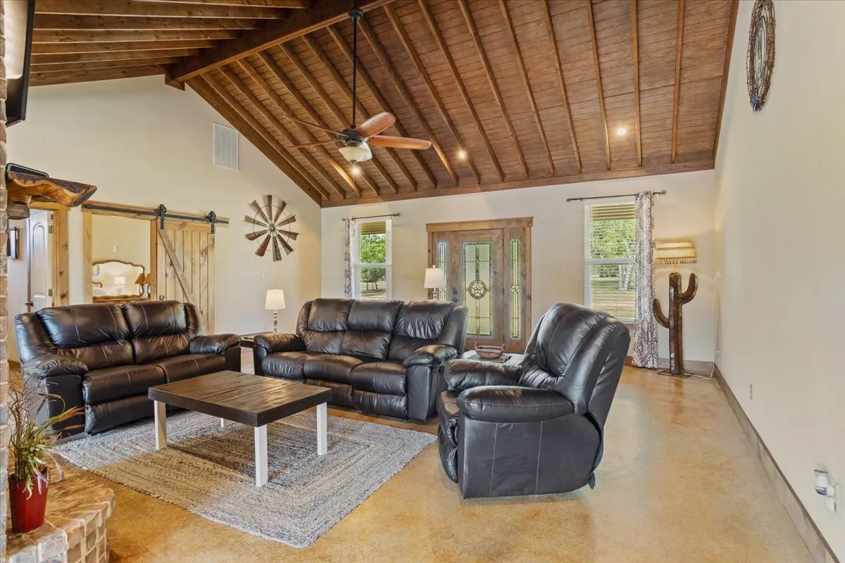 Spacious living area featuring a vaulted wood-finish ceiling, exposed beams, a ceiling fan, stained concrete flooring, and a barn door entry