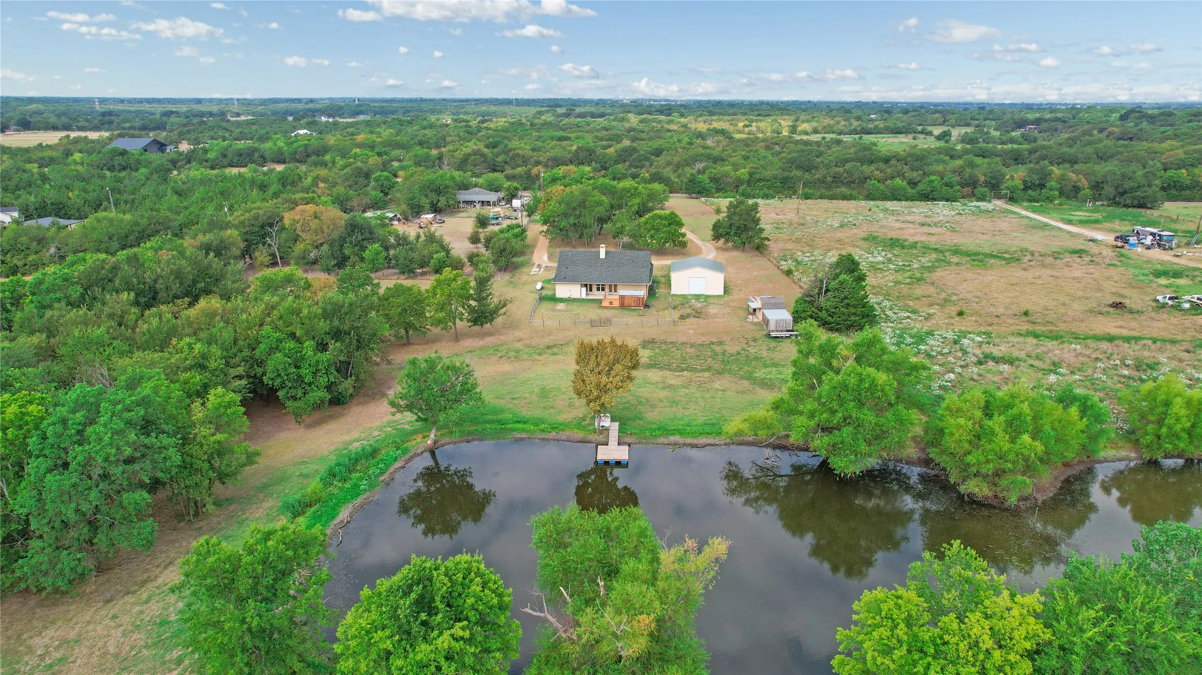 Expansive property featuring a tranquil pond with a pier, surrounded by mature trees