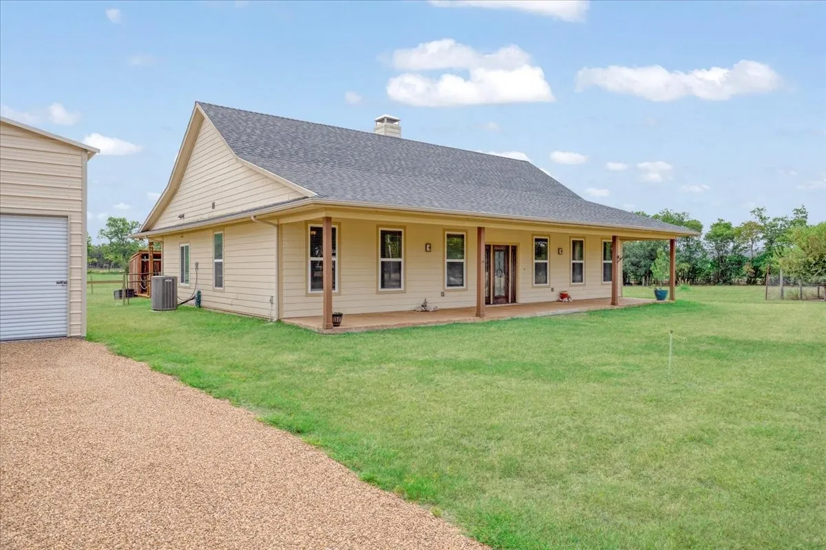 Ranch-style residence featuring a covered front porch with wood-finish columns, a gravel driveway, and an expansive lawn