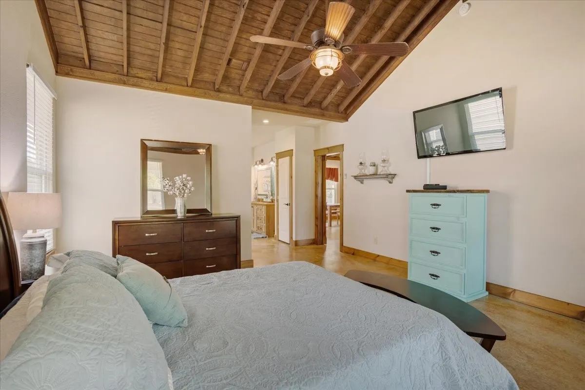 Vaulted wood-plank ceiling featuring exposed beams and a ceiling fan