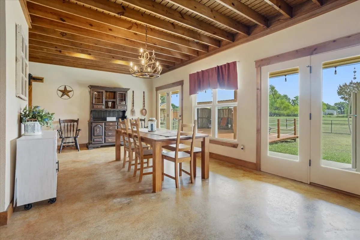 Dining area featuring an exposed wood beam ceiling, expansive floor-to-ceiling windows, and double French doors opening to the exterior