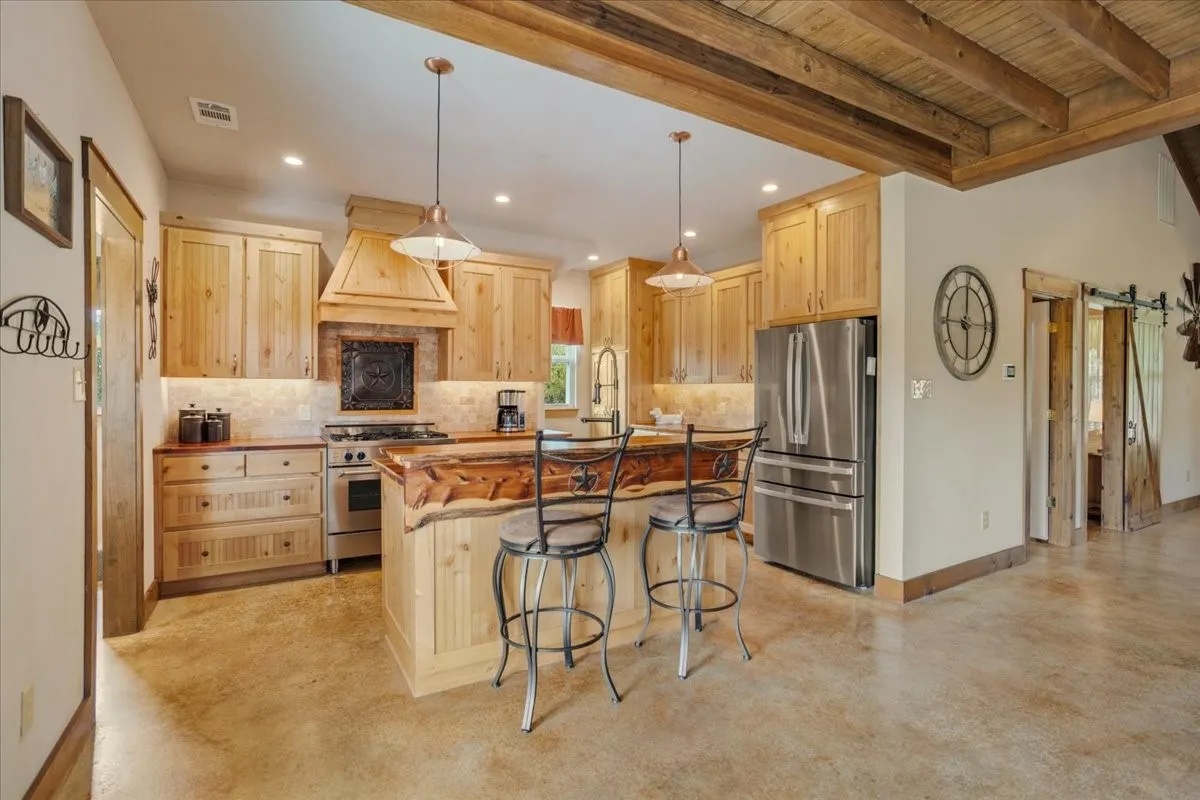 Open-concept kitchen featuring wood cabinetry, stainless steel appliances, a central island with a live-edge countertop, and pendant lighting