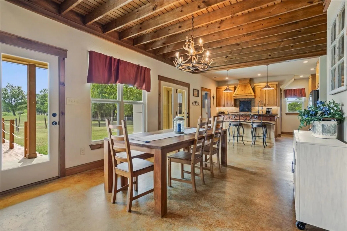 Open-concept living space featuring wood-finish ceiling beams, expansive windows, and stained concrete flooring