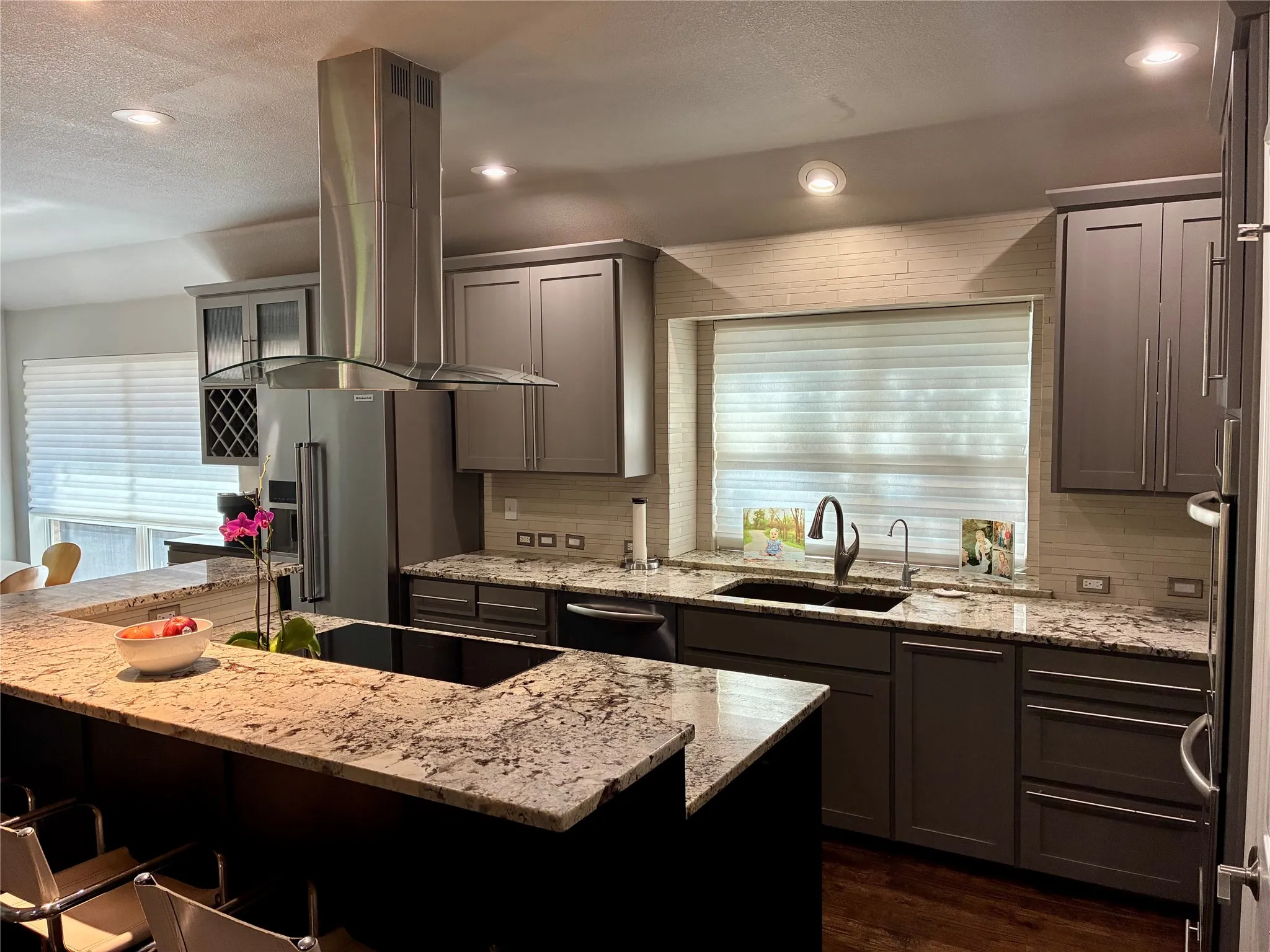 Gourmet kitchen featuring a central island with an integrated cooktop, granite countertops, gray cabinetry, a stainless steel range hood, and recessed lighting