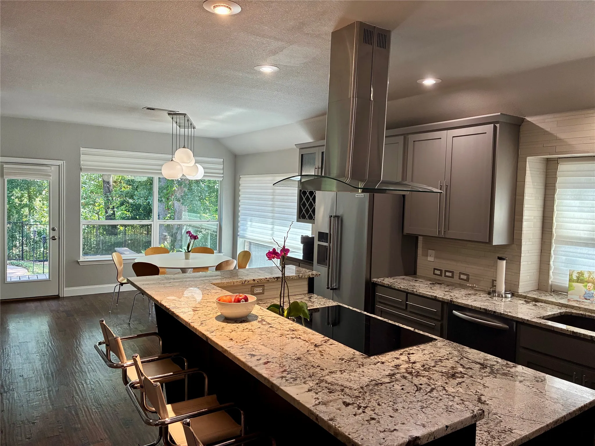 Kitchen featuring a large island with integrated cooktop, stone countertops, stainless steel appliances, contemporary cabinetry, and wood-finish flooring