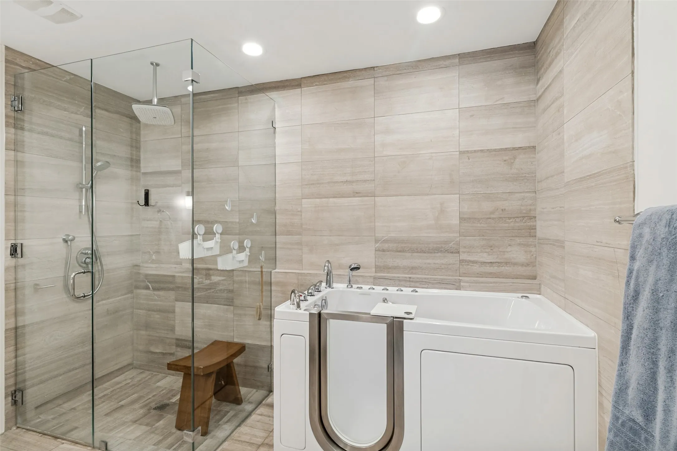 Bathroom featuring a walk-in tub, a glass-enclosed shower with a rainfall showerhead, a handheld shower fixture, and light-toned tile walls and flooring