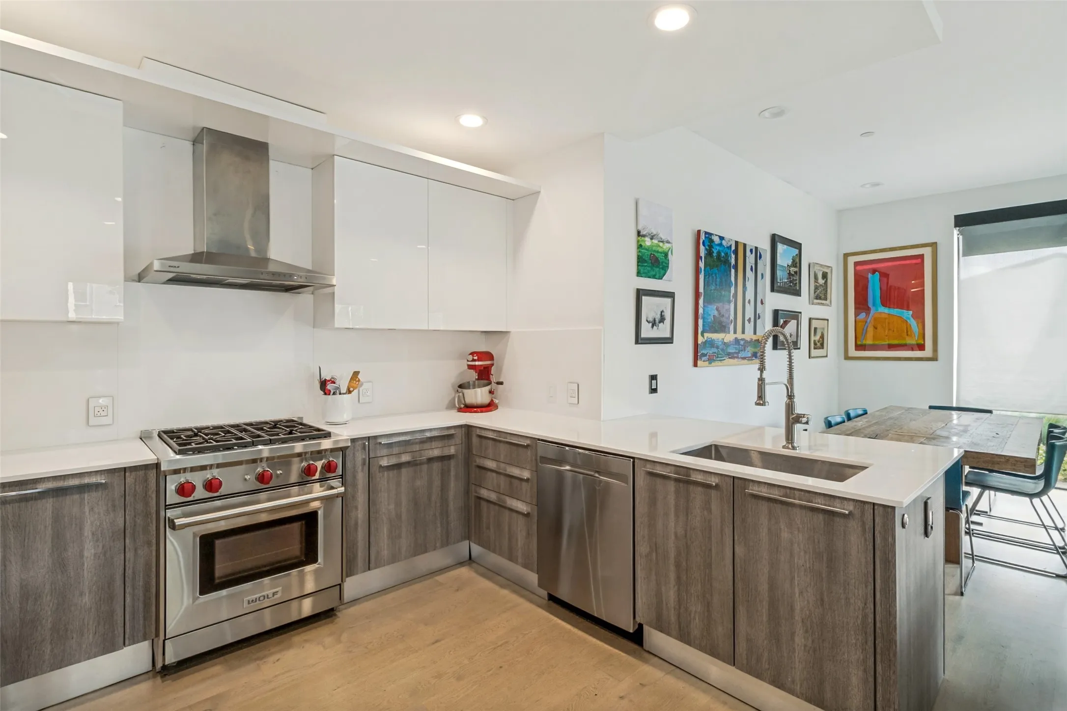 Modern kitchen featuring stainless steel appliances, wood-finish lower cabinetry, white upper cabinetry, and a white countertop