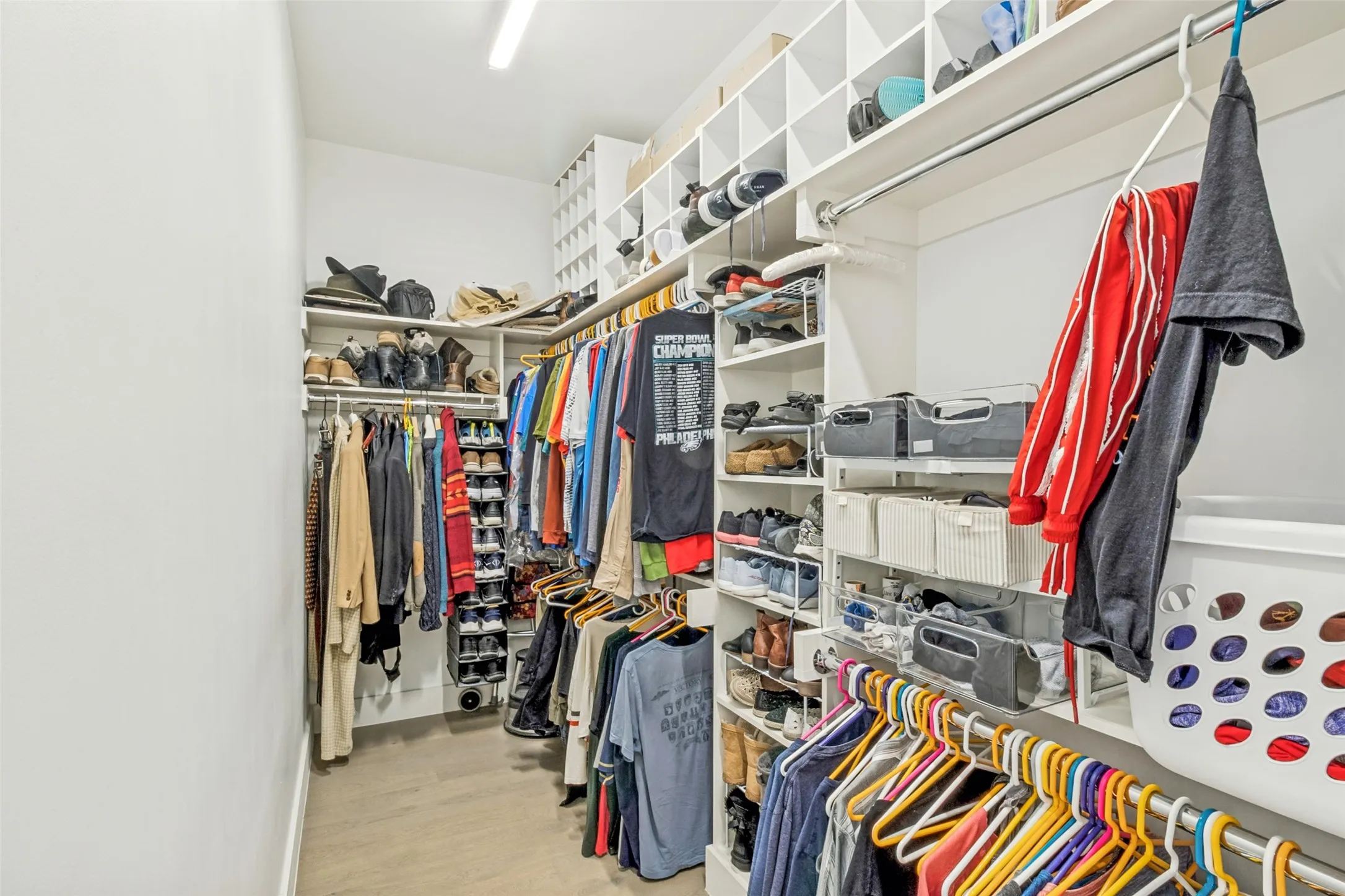 Walk-in closet featuring custom shelving, multiple hanging rods, built-in shoe racks, and wood-finish flooring