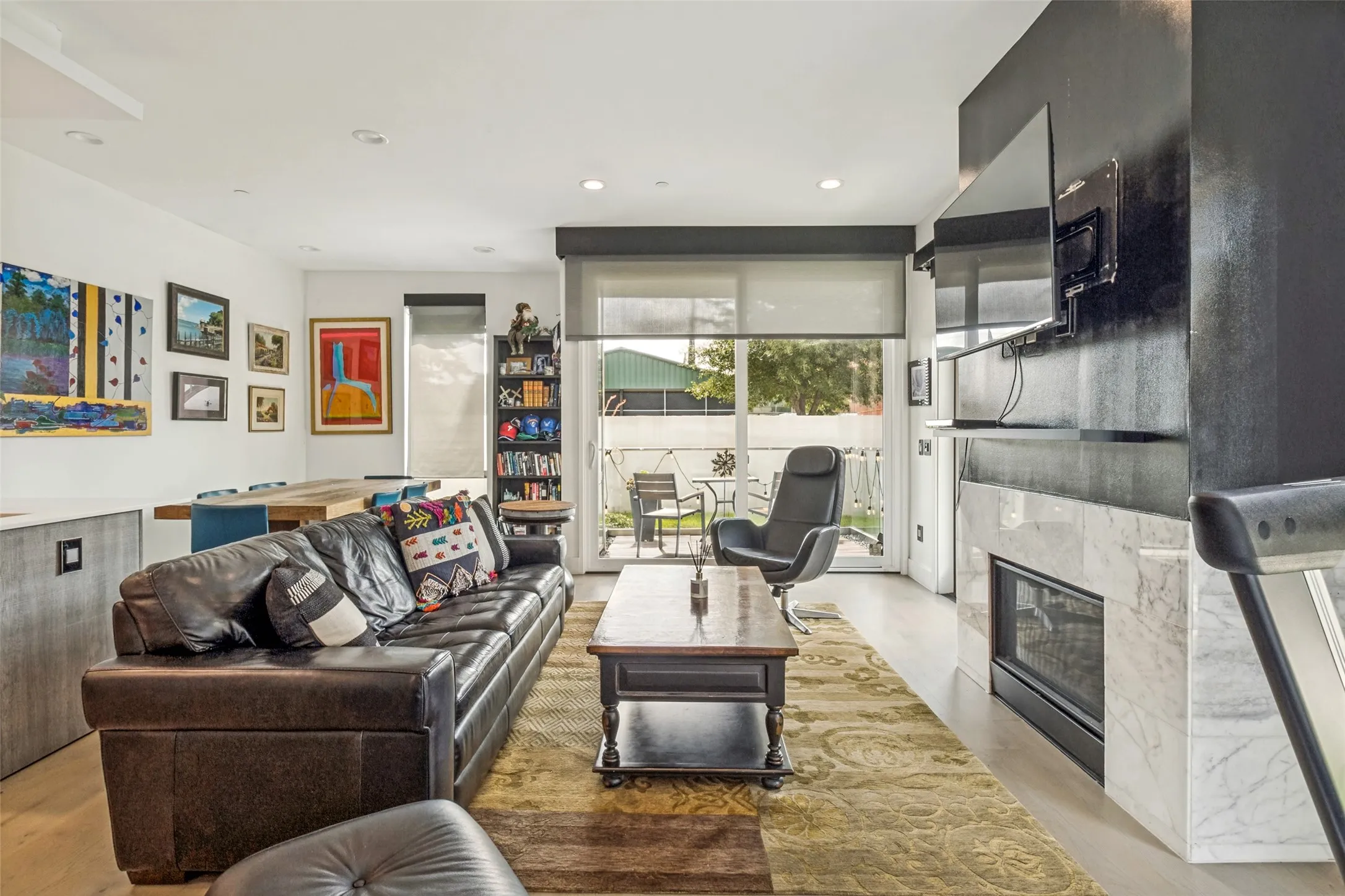 Open-concept living area featuring light wood-finish flooring, recessed lighting, and a modern fireplace with a stone surround