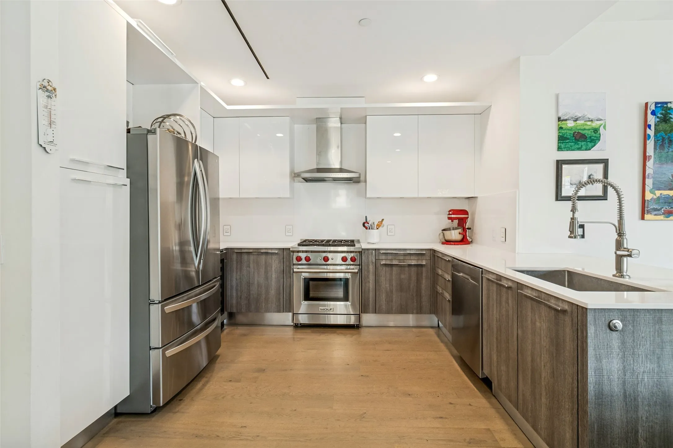 Modern kitchen featuring wood-finish lower cabinetry, white upper cabinetry, stainless steel appliances, and light-toned countertops