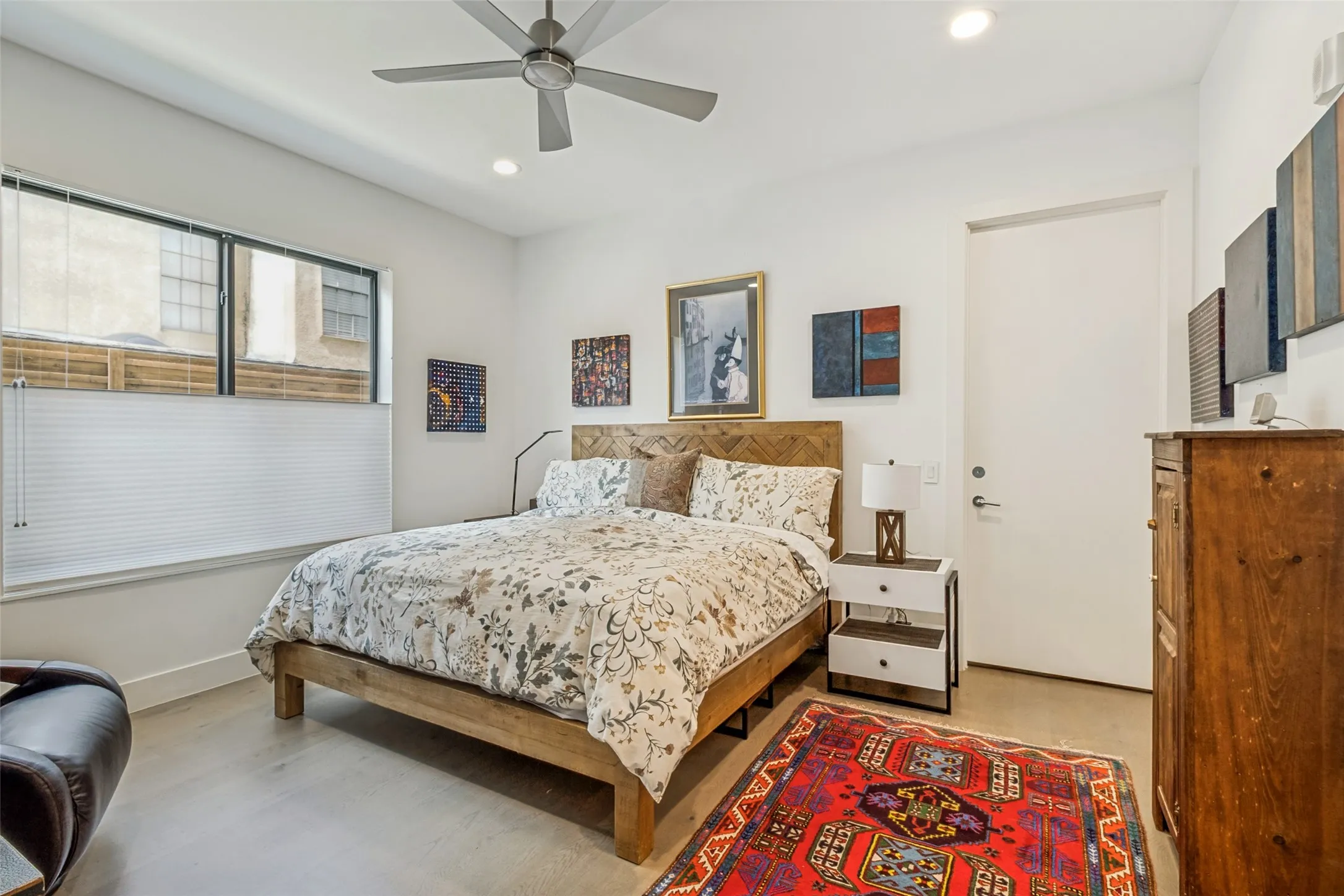 Bedroom featuring a ceiling fan with integrated lighting, recessed ceiling lighting, a large window with privacy blinds, a solid core door, and wood-finish flooring