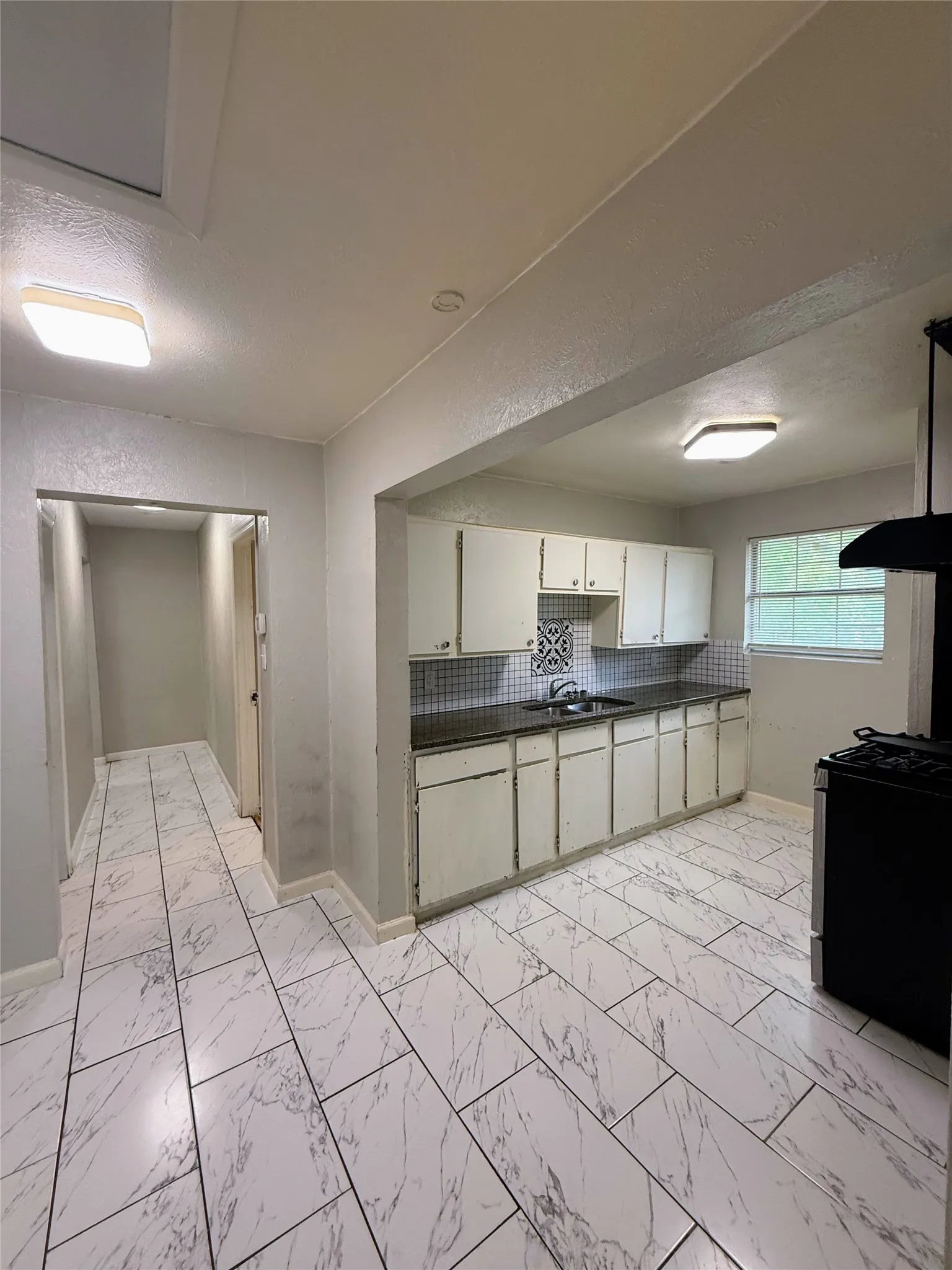 Kitchen featuring white cabinetry, dark countertops, and a white tile backsplash