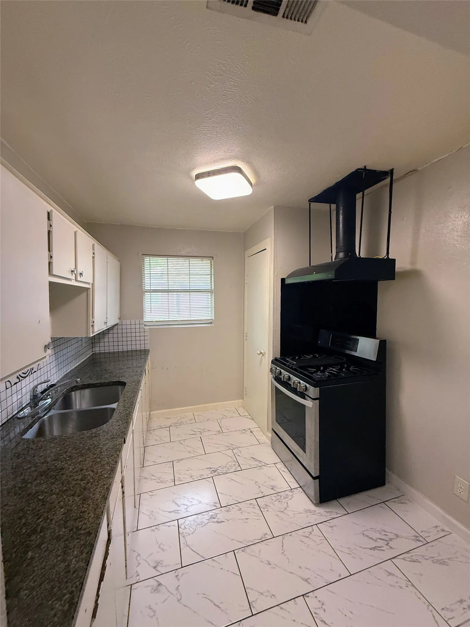 Kitchen featuring white cabinetry, a dual basin stainless steel sink, dark speckled countertops, and a subway tile backsplash