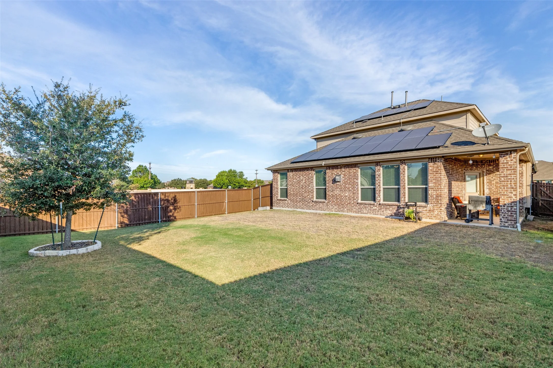 Back of house with a patio area, a lawn, and solar panels