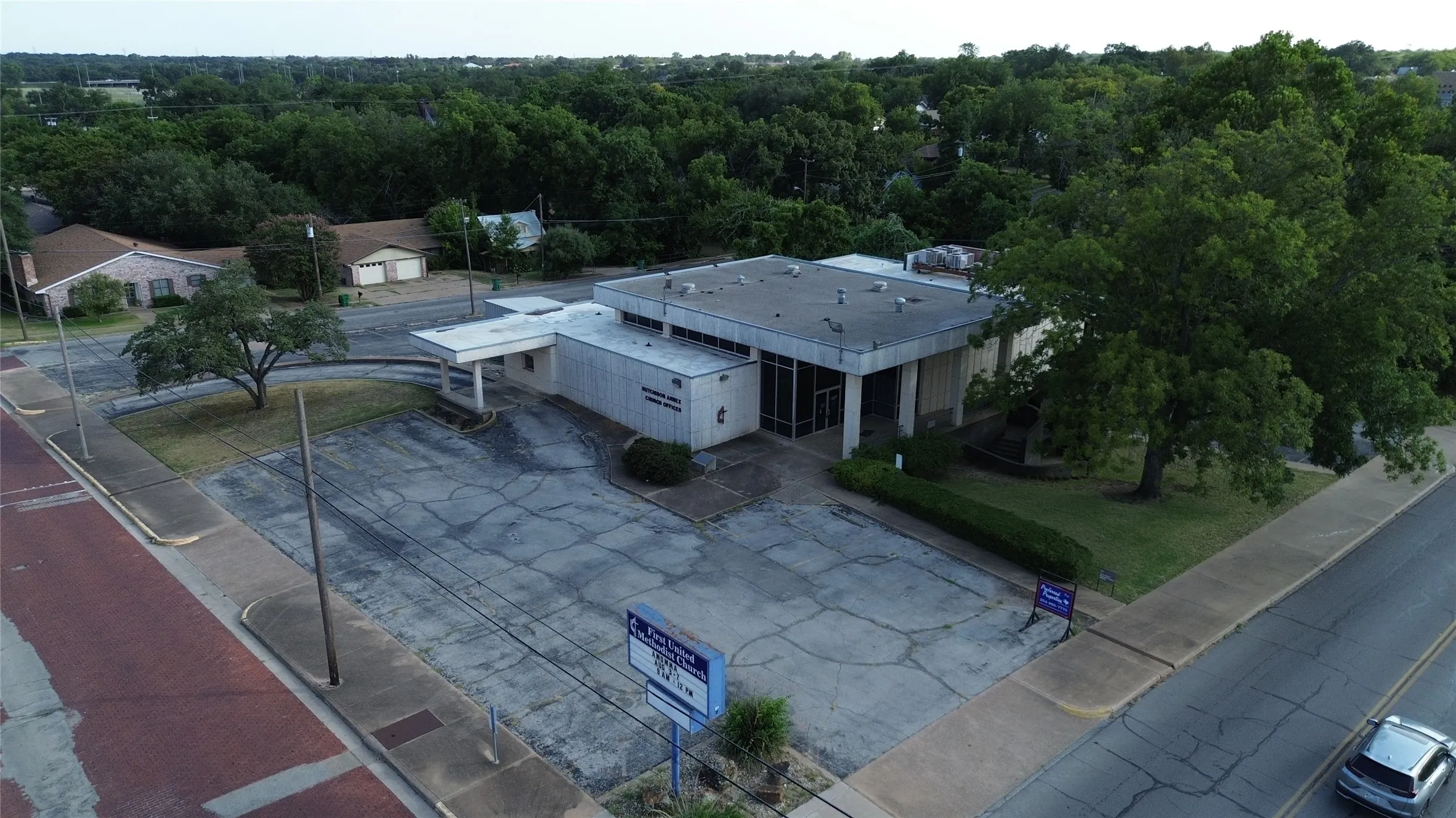 Single-story commercial building with an expansive paved lot and mature trees