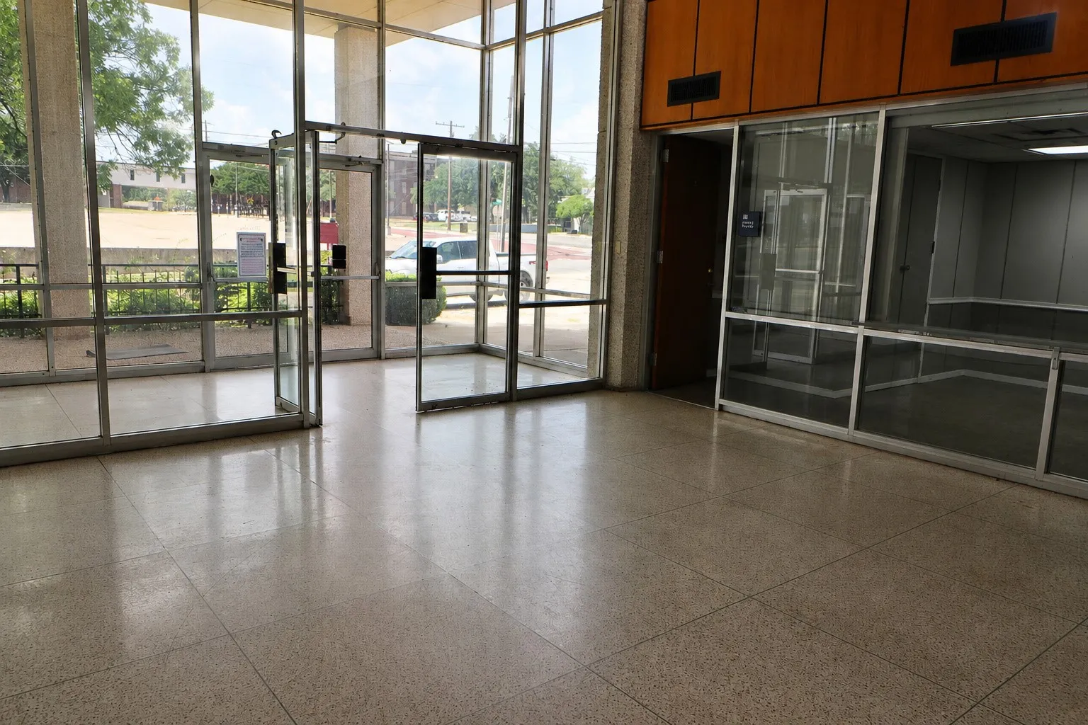Expansive tiled flooring, a glass-paneled entrance with double doors, and a partial wall with wood-finish paneling and transom windows