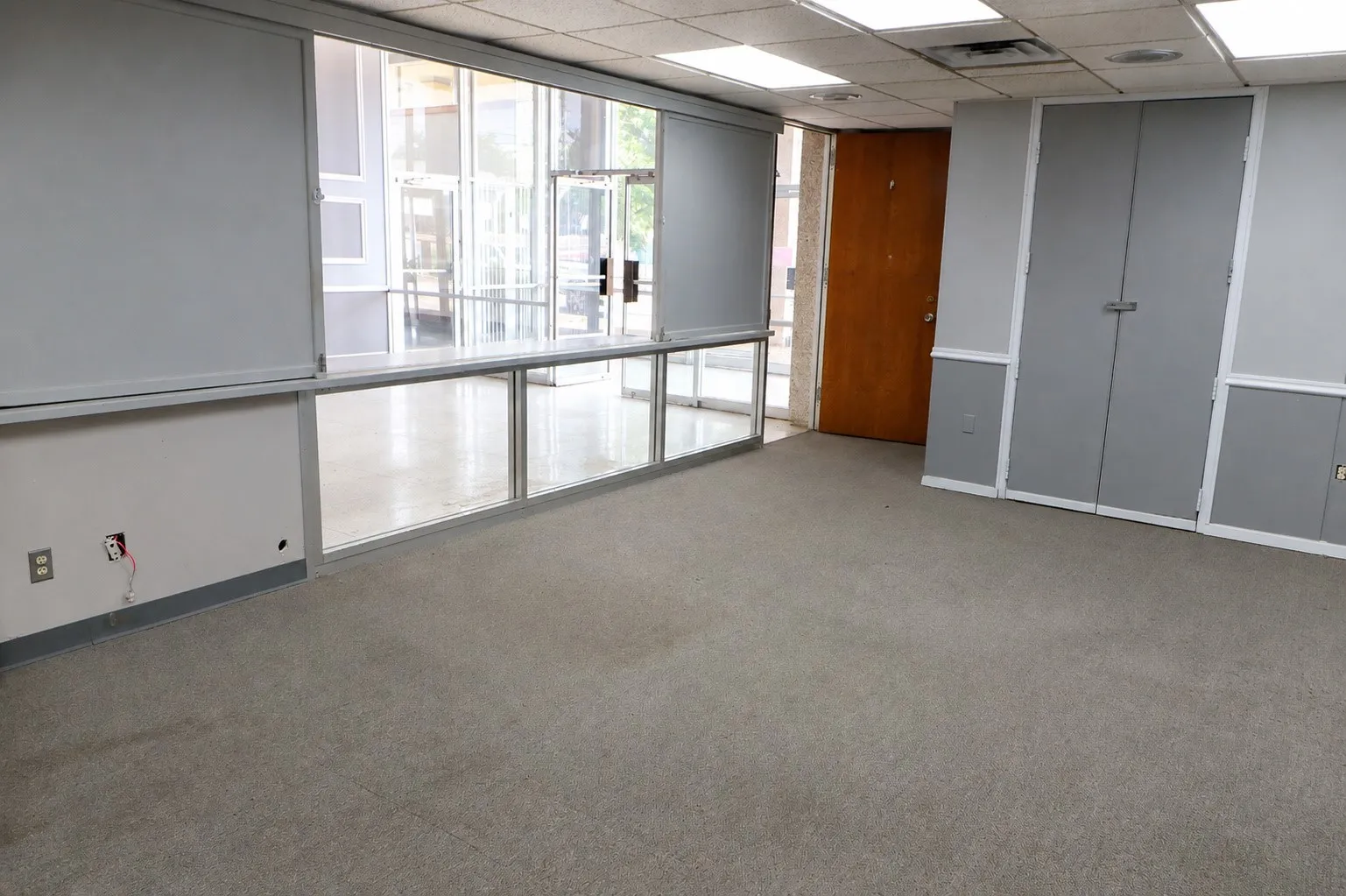 Gray carpeting with a drop ceiling, featuring a wood-finish door, and integrated storage units