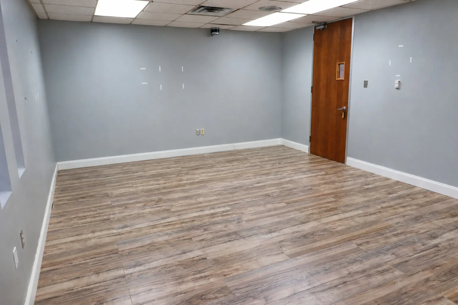 Wood-finish flooring with white trim, light gray walls, and a recessed ceiling with integrated lighting