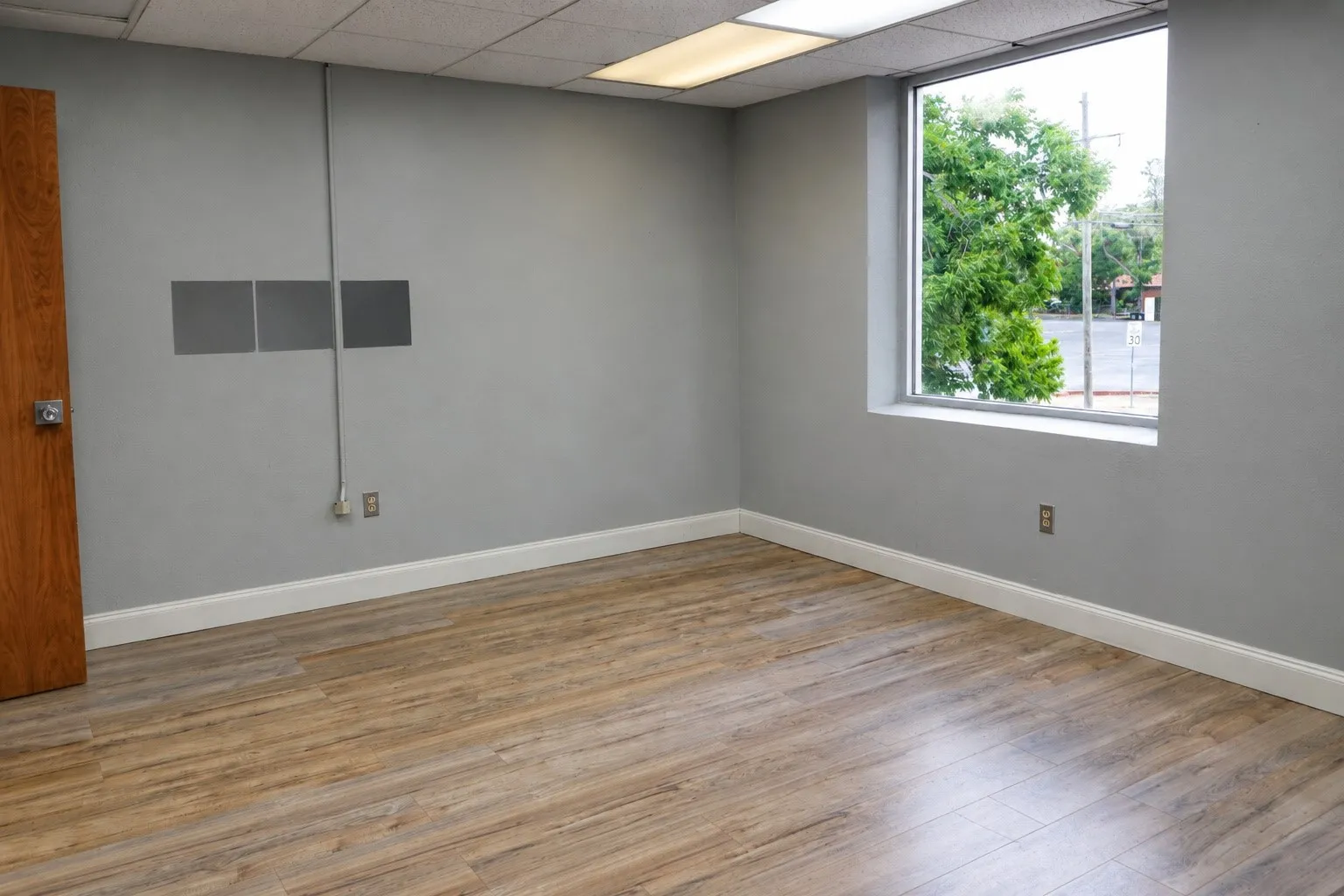 Wood-finish flooring, light grey painted walls, white trim, recessed lighting, and a large window