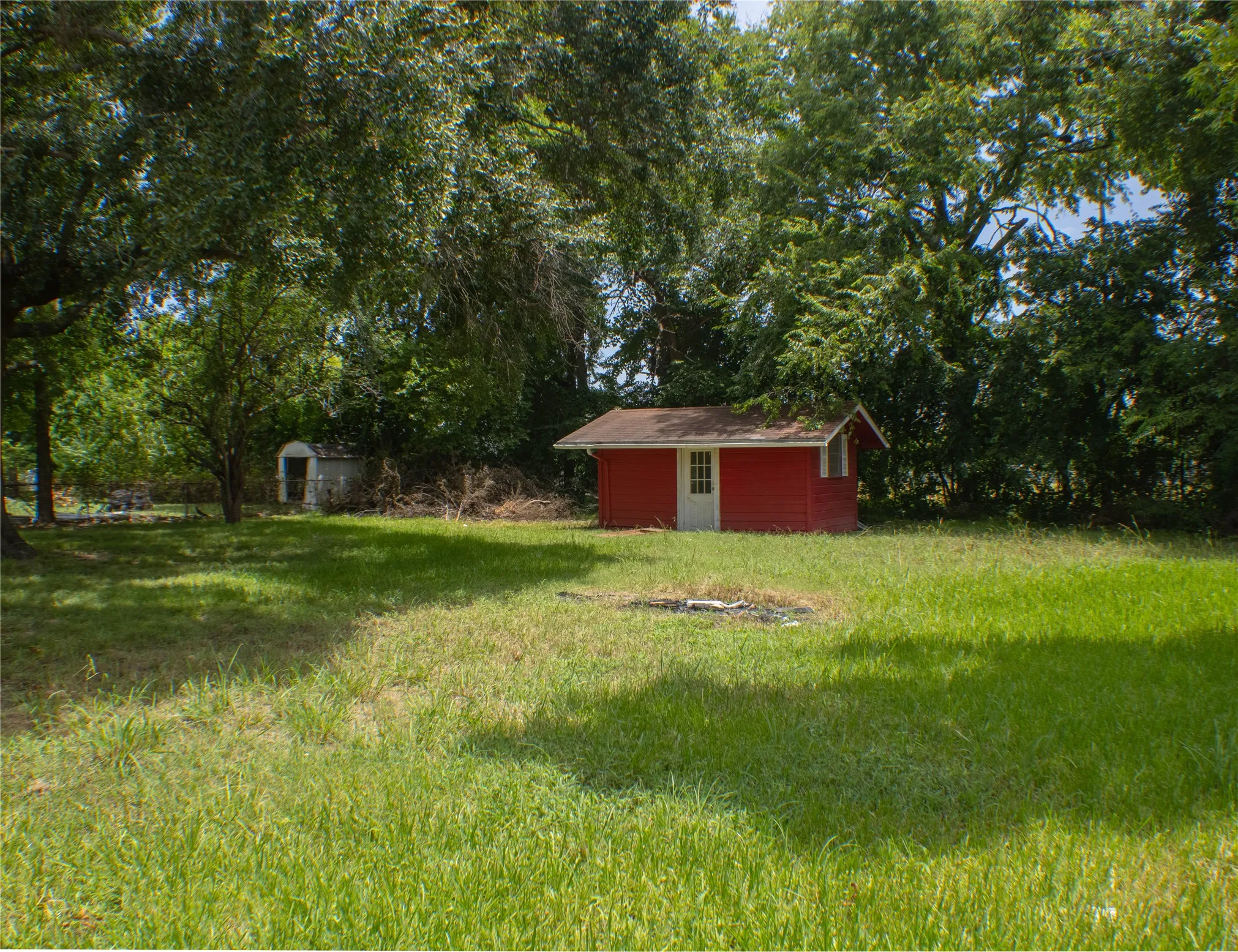 Expansive green space featuring a red outbuilding with white trim and a gabled roof
