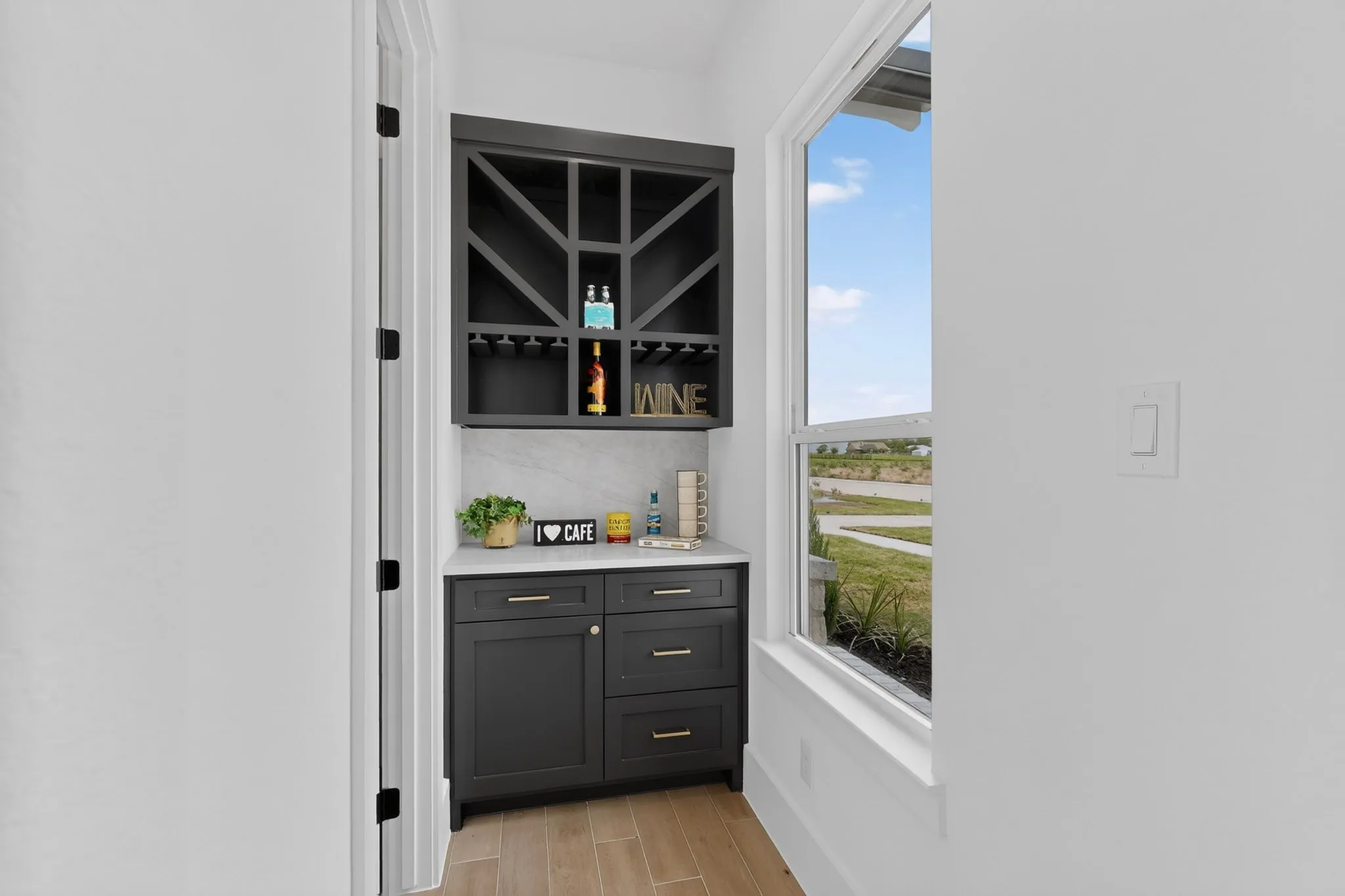 Built-in beverage station featuring dark cabinetry with gold hardware, a white countertop, and a geometrically patterned upper cabinet with integrated glass stemware racks