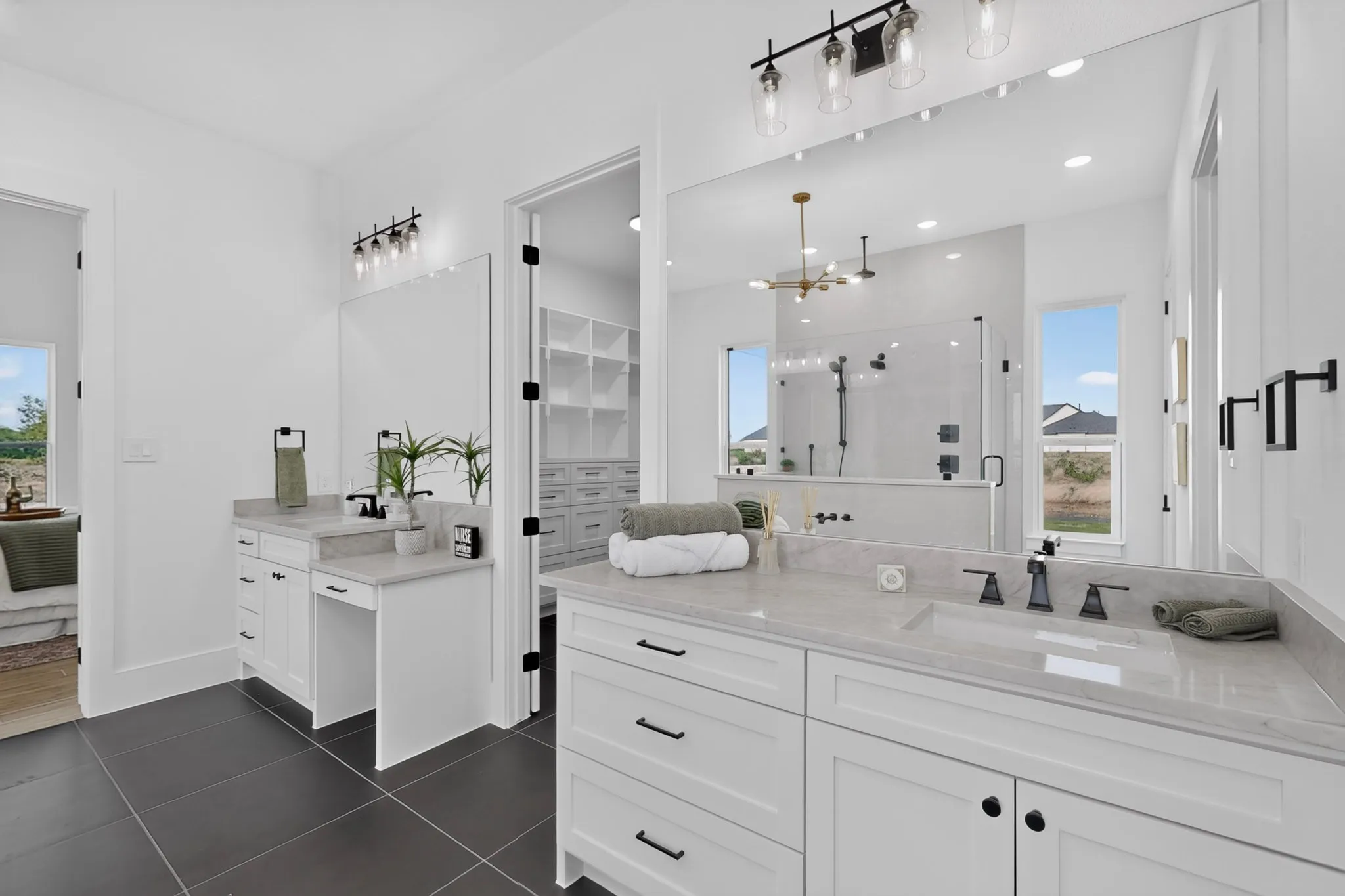Spacious bathroom featuring twin vanities with light-toned countertops, contrasting dark tile flooring, and a large frameless mirror