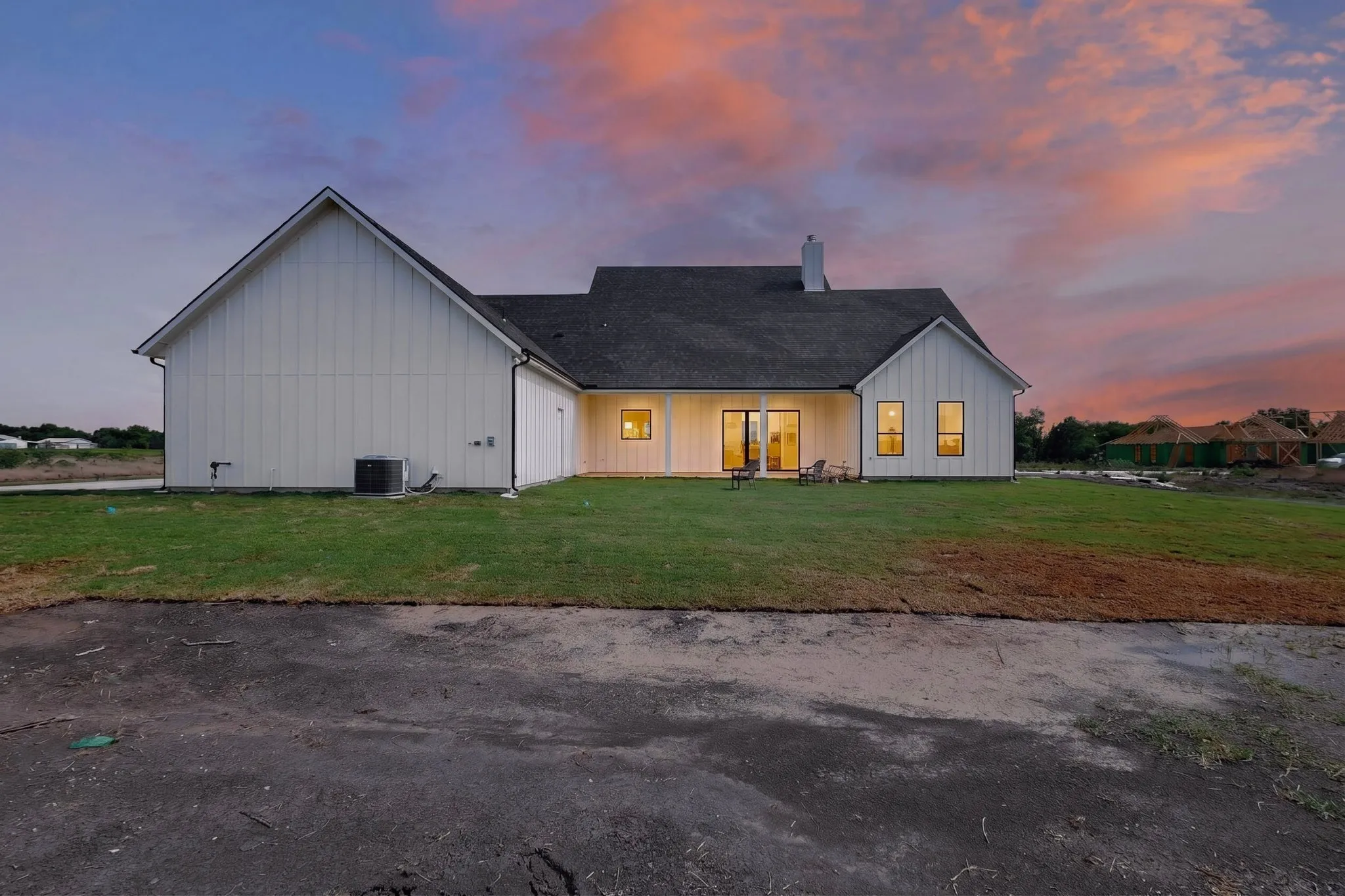 Rear exterior featuring white board-and-batten siding, a dark shingled roof, a covered patio area, and multiple windows