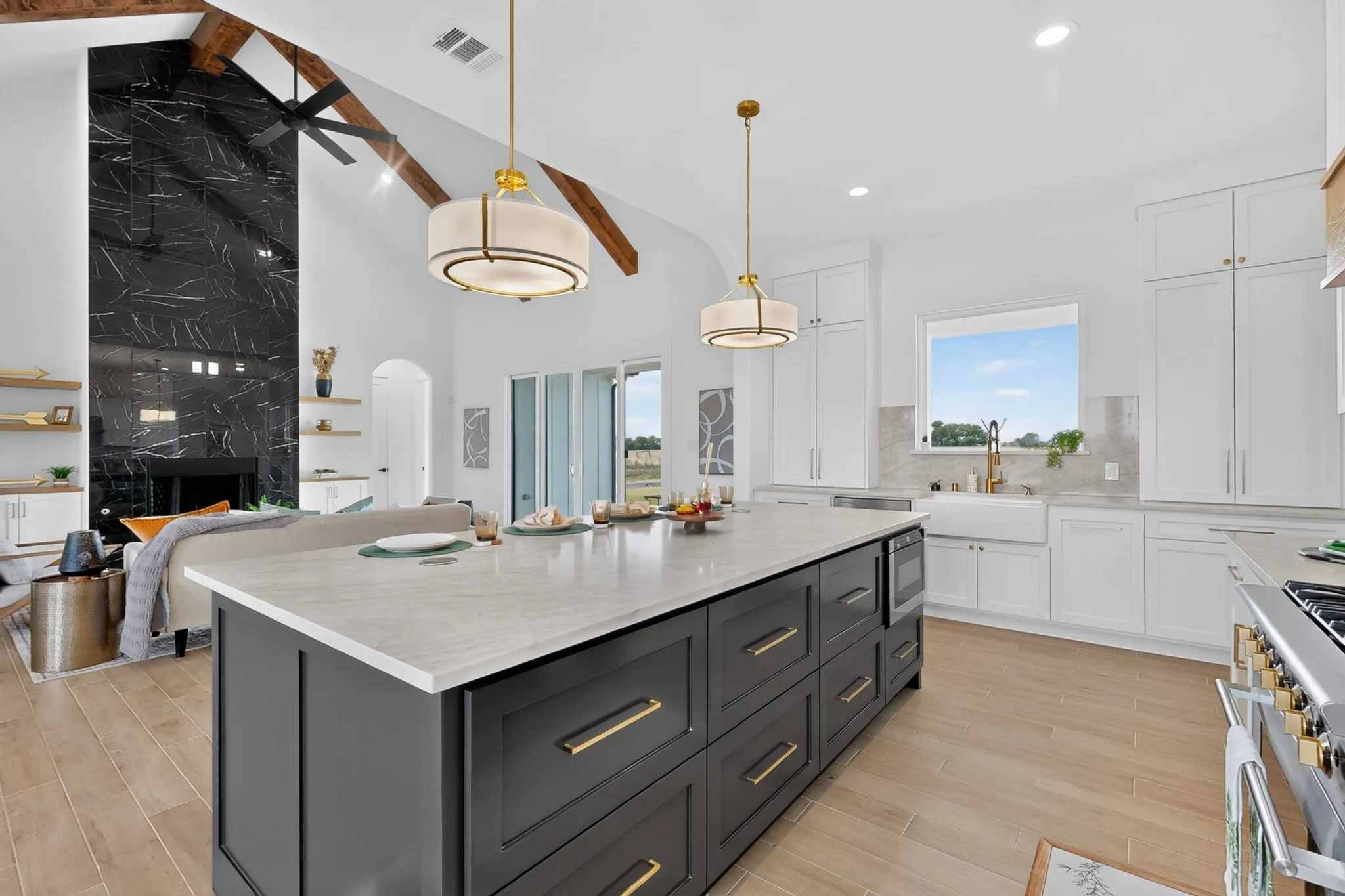 Expansive kitchen featuring a large central island with a light-toned countertop and dark cabinetry, wood-finish flooring, and white upper and lower perimeter cabinetry