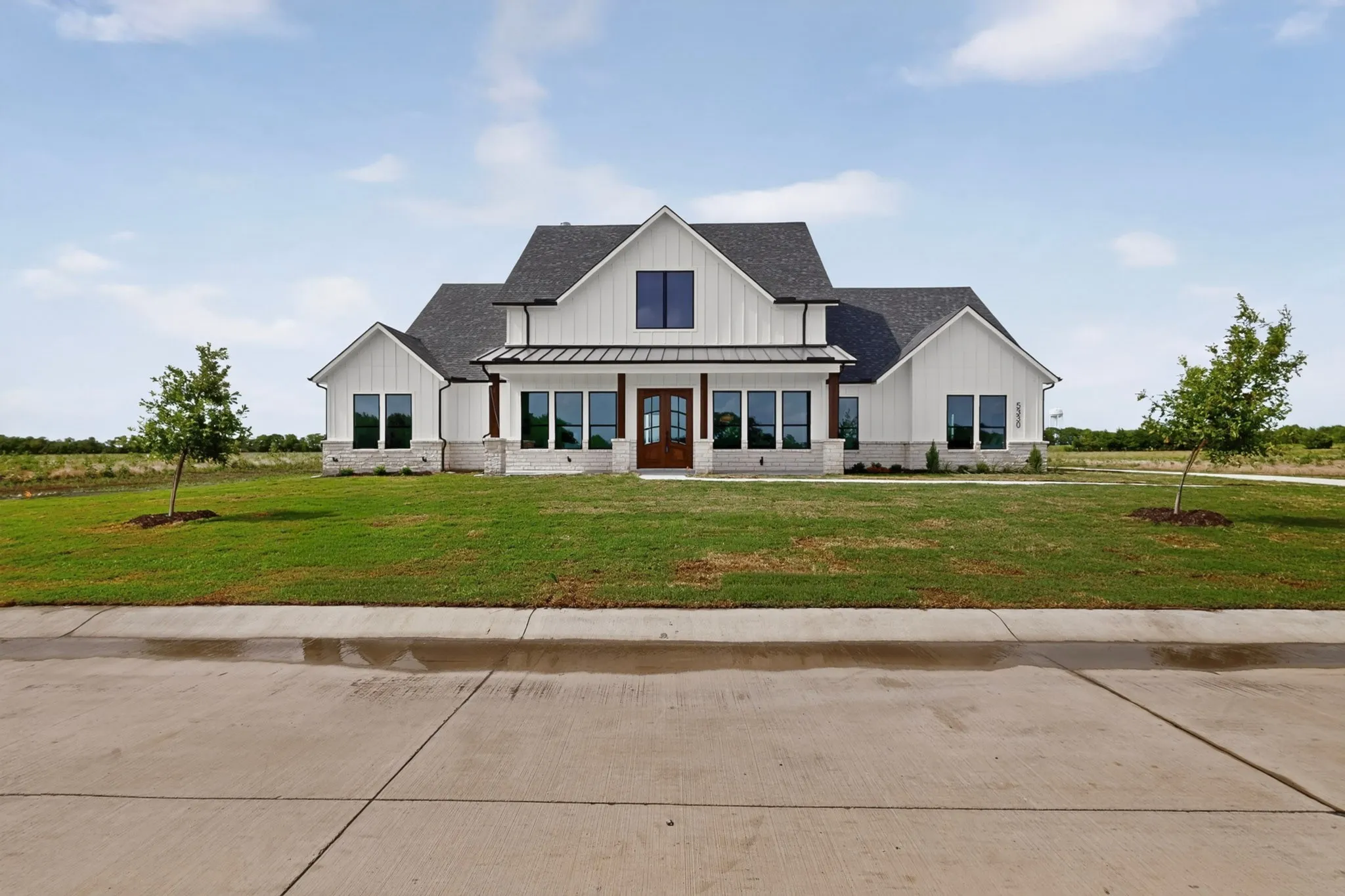 Modern farmhouse exterior featuring white board-and-batten siding, a dark shingled roof, a covered entry with wood-tone columns, and a stone-clad foundation