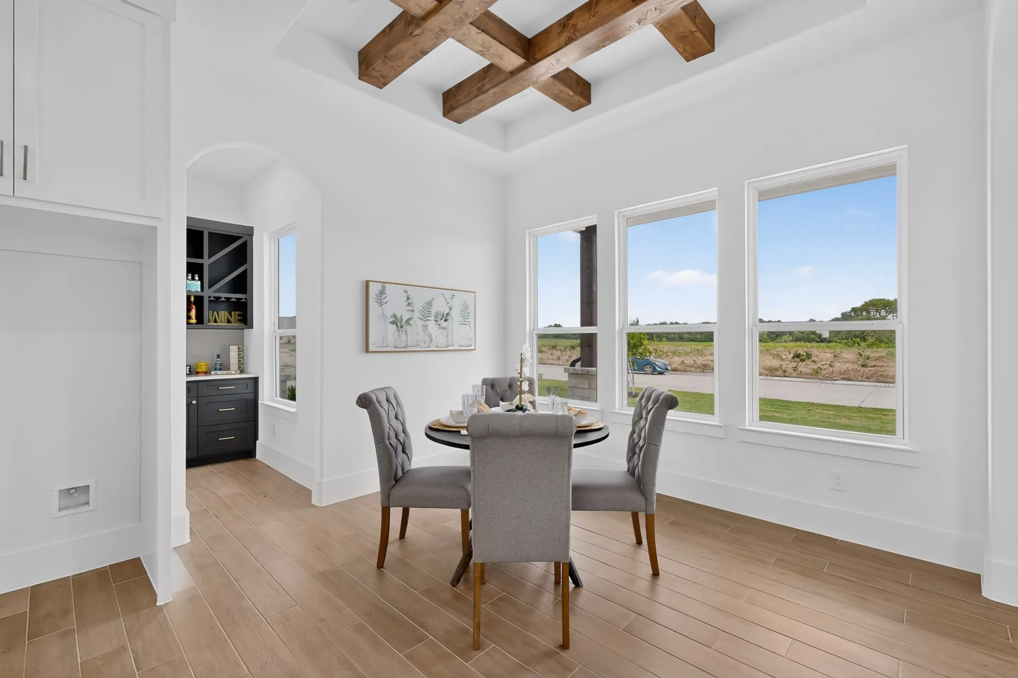 Spacious dining area featuring wood-finish flooring, a coffered ceiling with exposed wood beams, and three large windows