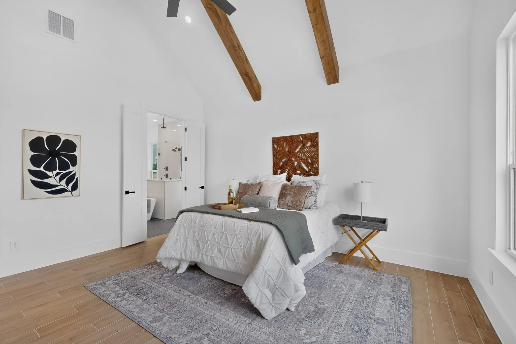 Spacious room featuring vaulted ceilings with exposed wood beams, wood-finish flooring, a large window, and an en-suite bathroom with a glass-enclosed shower