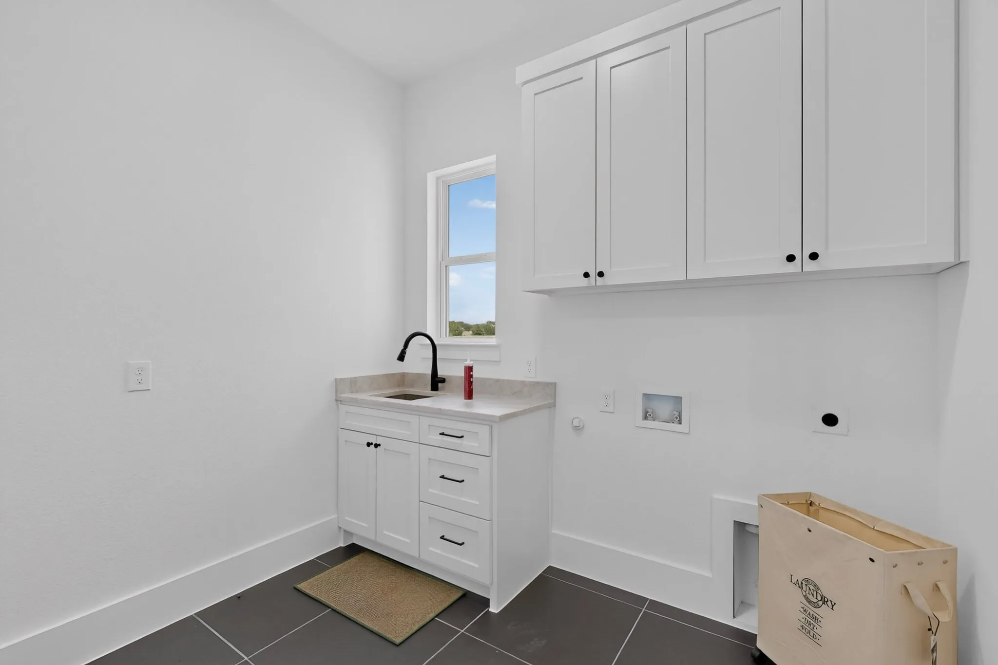 Laundry room featuring white shaker cabinetry, an integrated sink with a matte black faucet, and a light-colored countertop