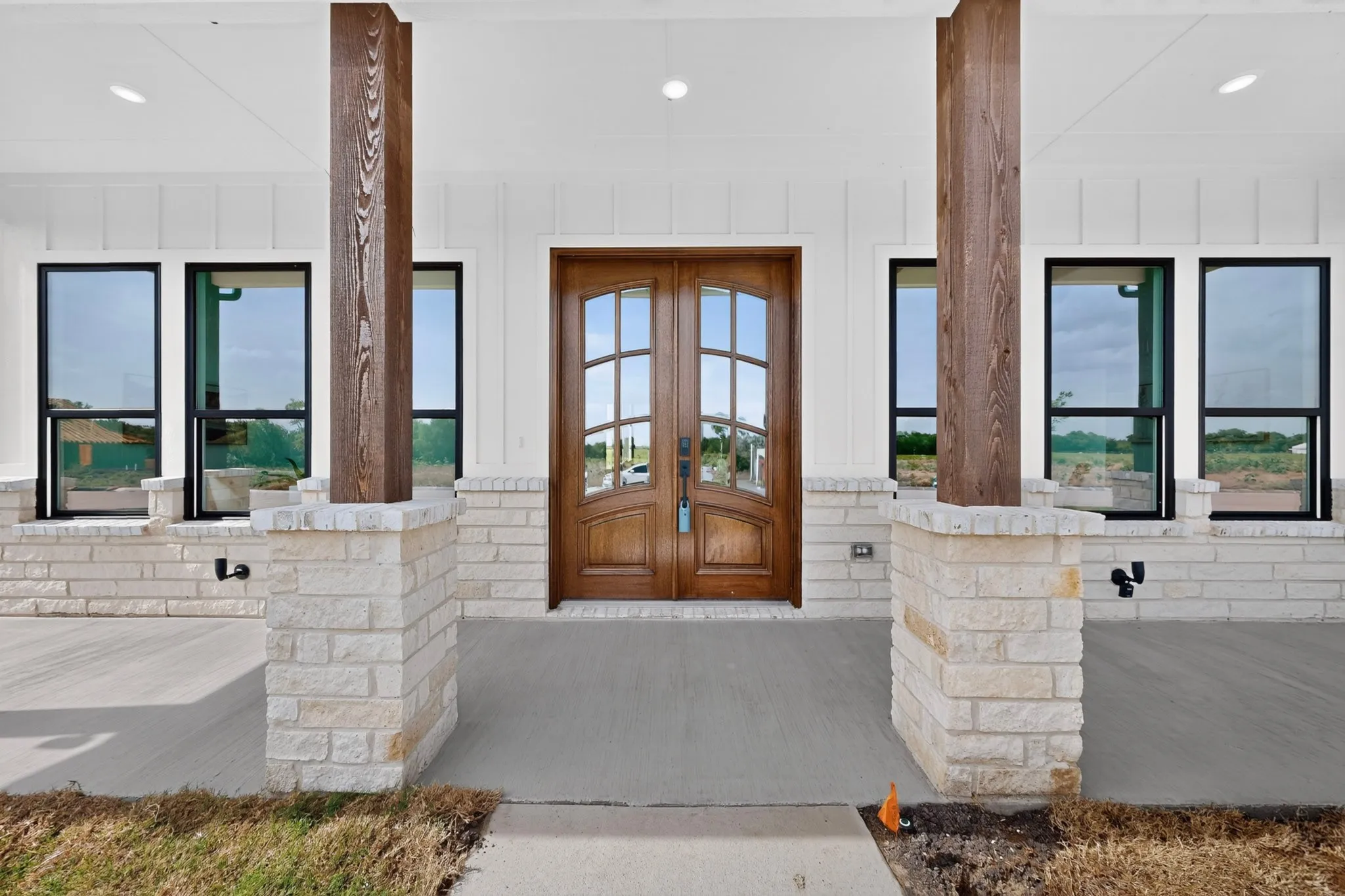 Entryway featuring double wooden doors with arched glass inserts, framed by white board-and-batten siding