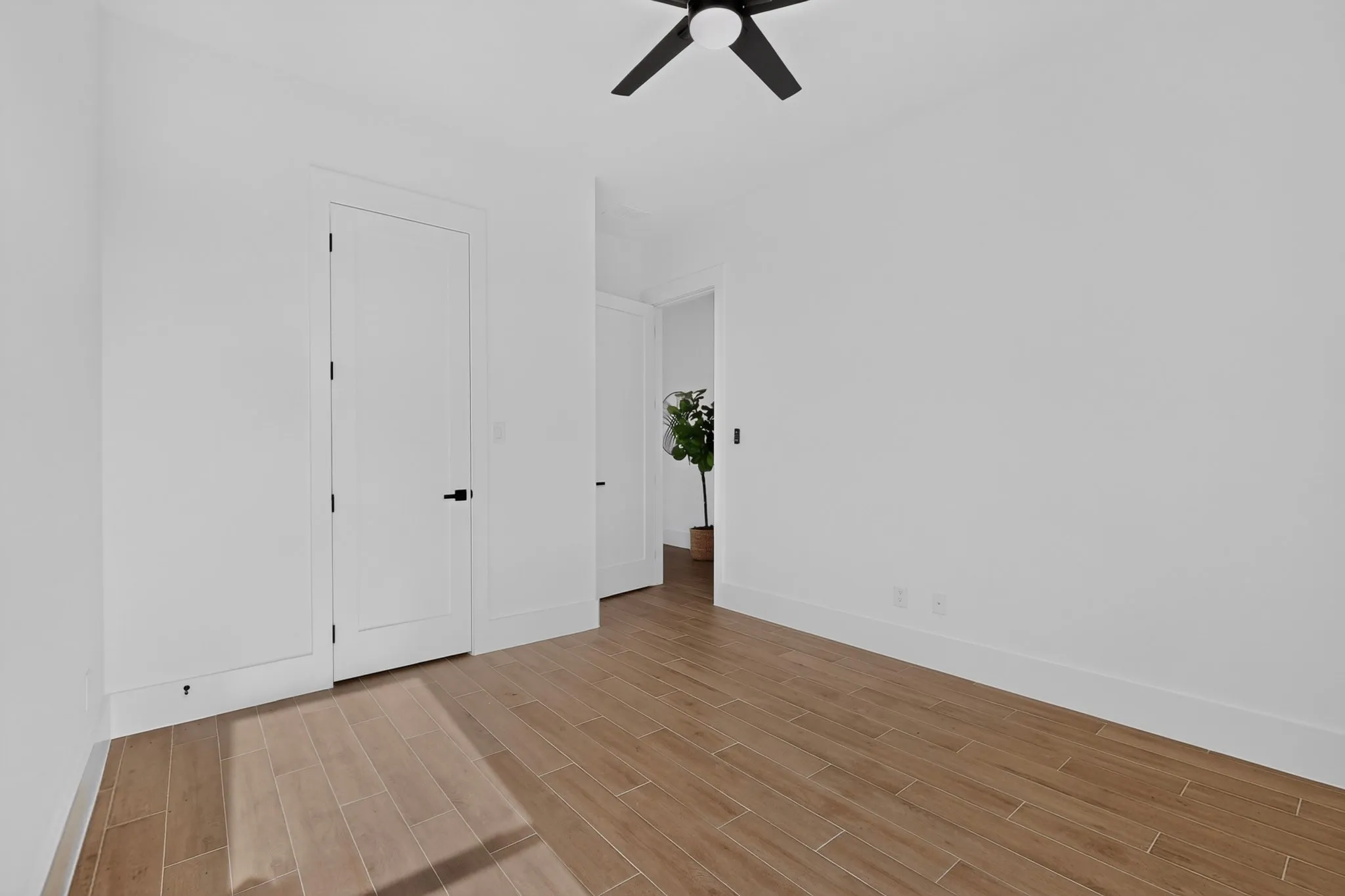 Room featuring wood-finish flooring, crisp white walls, and a contemporary black ceiling fan