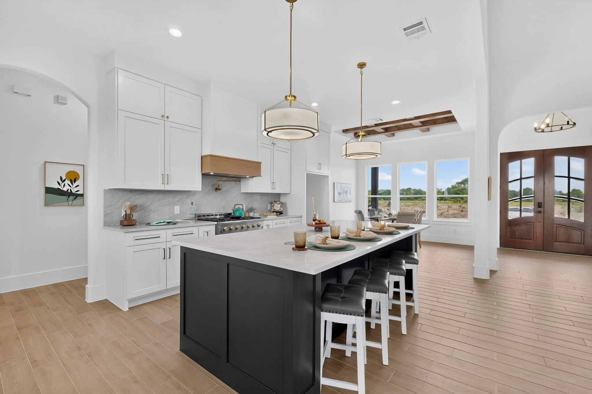 Open-concept kitchen featuring an expansive center island with seating, white shaker cabinetry, a wood-finish range hood, and light-tone wood-finish flooring