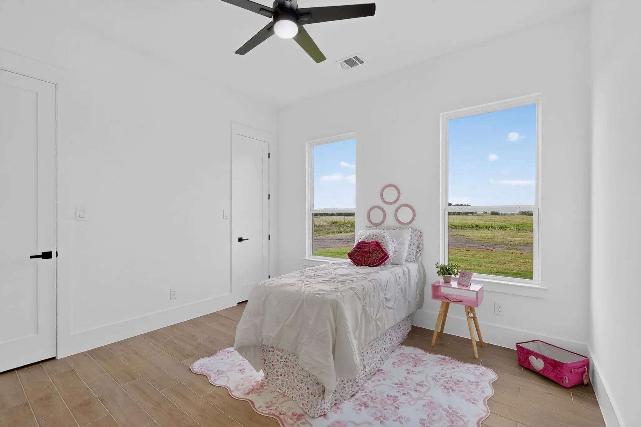 Bright room featuring wood-look flooring, two windows, two solid white doors with black hardware, and a ceiling fan with integrated lighting