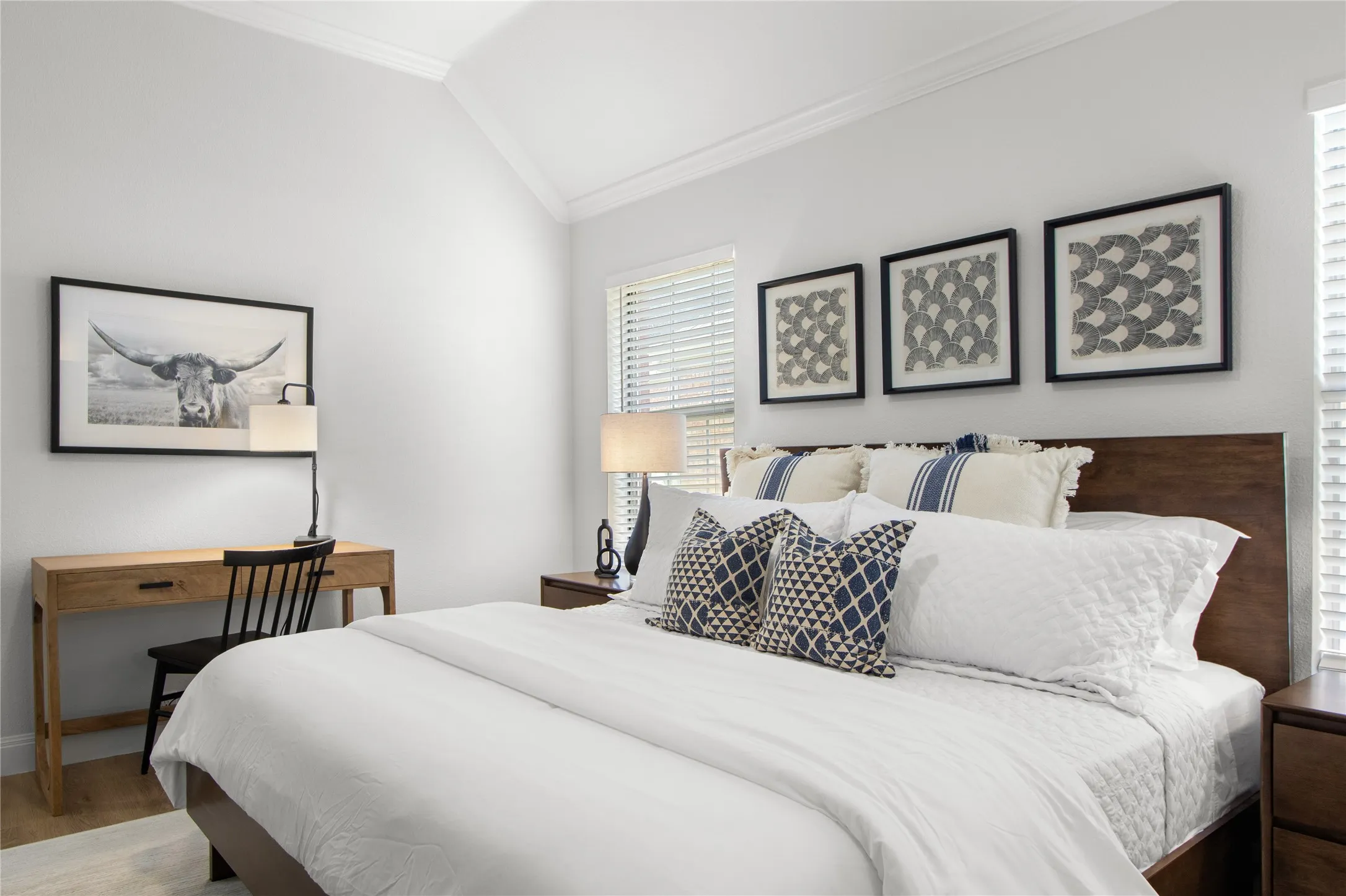 Vaulted ceiling with crown molding, natural light from a large window with horizontal blinds, wood-finish flooring, and a built-in wood headboard