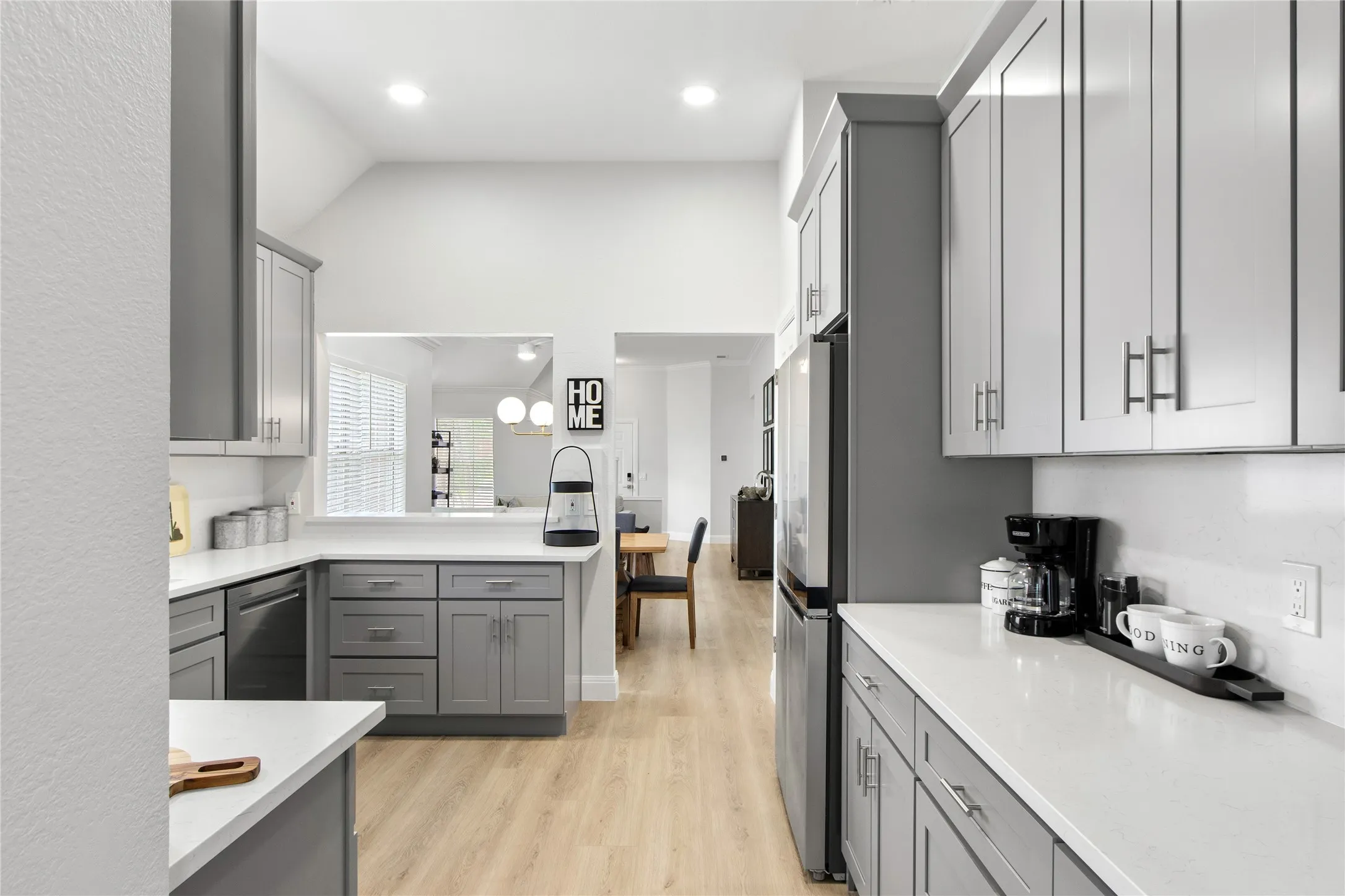 Modern kitchen featuring light wood-finish flooring, white countertops, and contemporary grey cabinetry with brushed nickel hardware