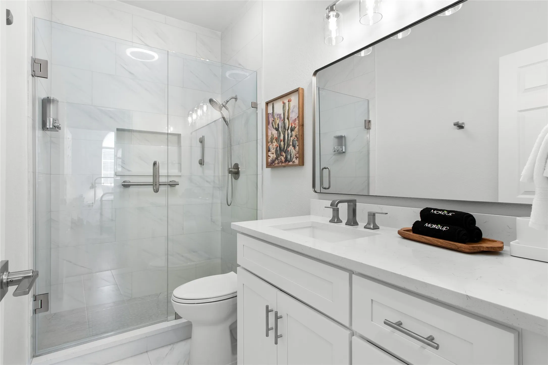 Sleek bathroom featuring a frameless glass shower enclosure with a built-in niche, white shaker-style vanity with a light-toned countertop, and a wide rectangular mirror with overhead lighting