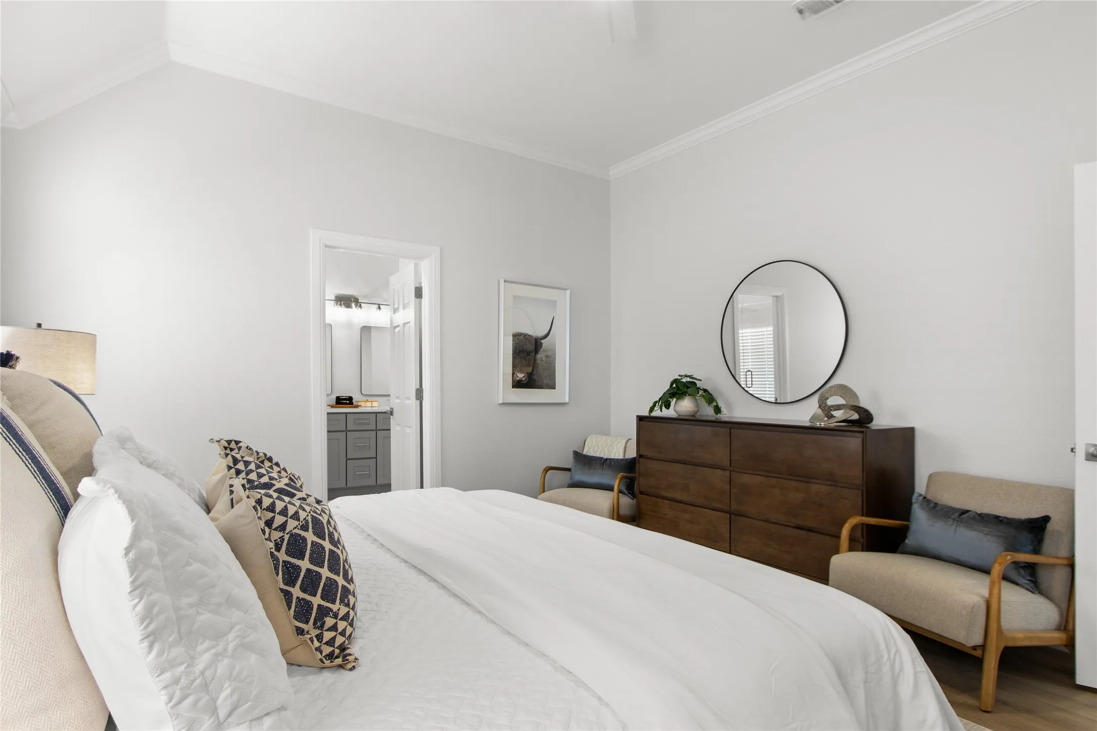 Vaulted ceiling with crown molding, light wood-finish flooring, and a doorway revealing a bathroom with a vanity and mirror