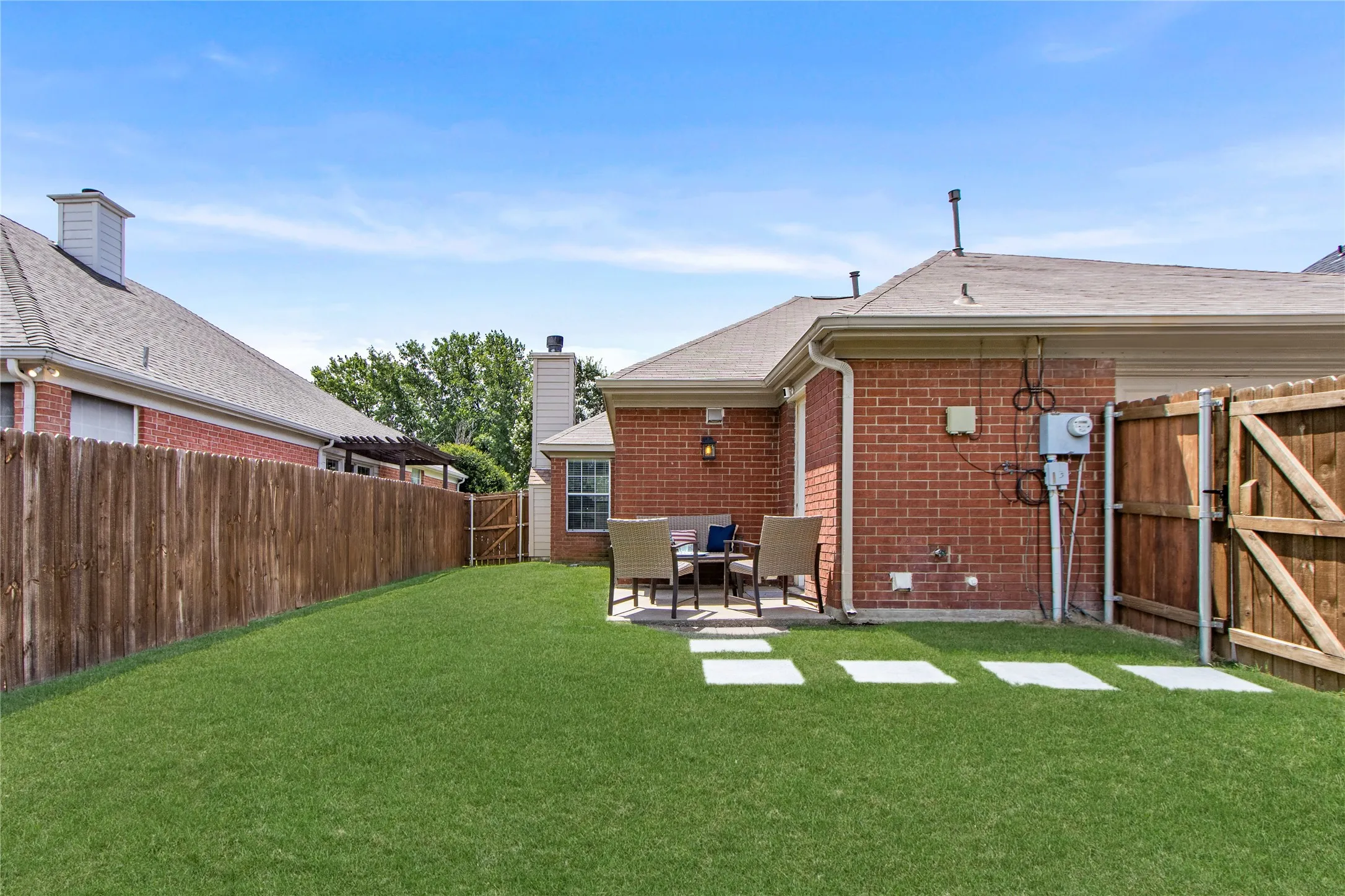 Spacious backyard featuring a lush lawn, concrete paver patio, brick exterior, and a privacy fence