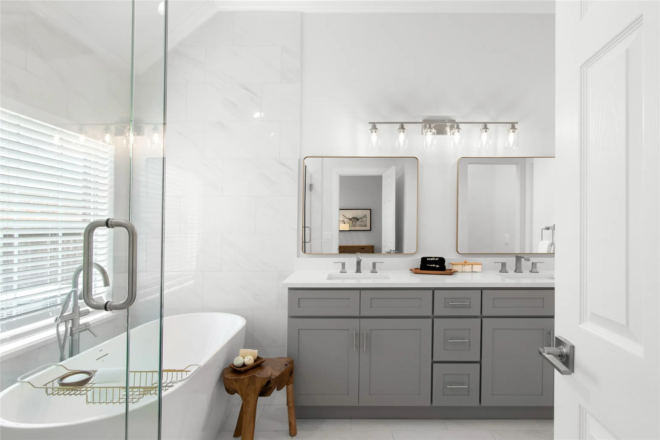 Bathroom featuring a freestanding soaking tub, clear glass shower enclosure, and a double vanity with gray cabinetry