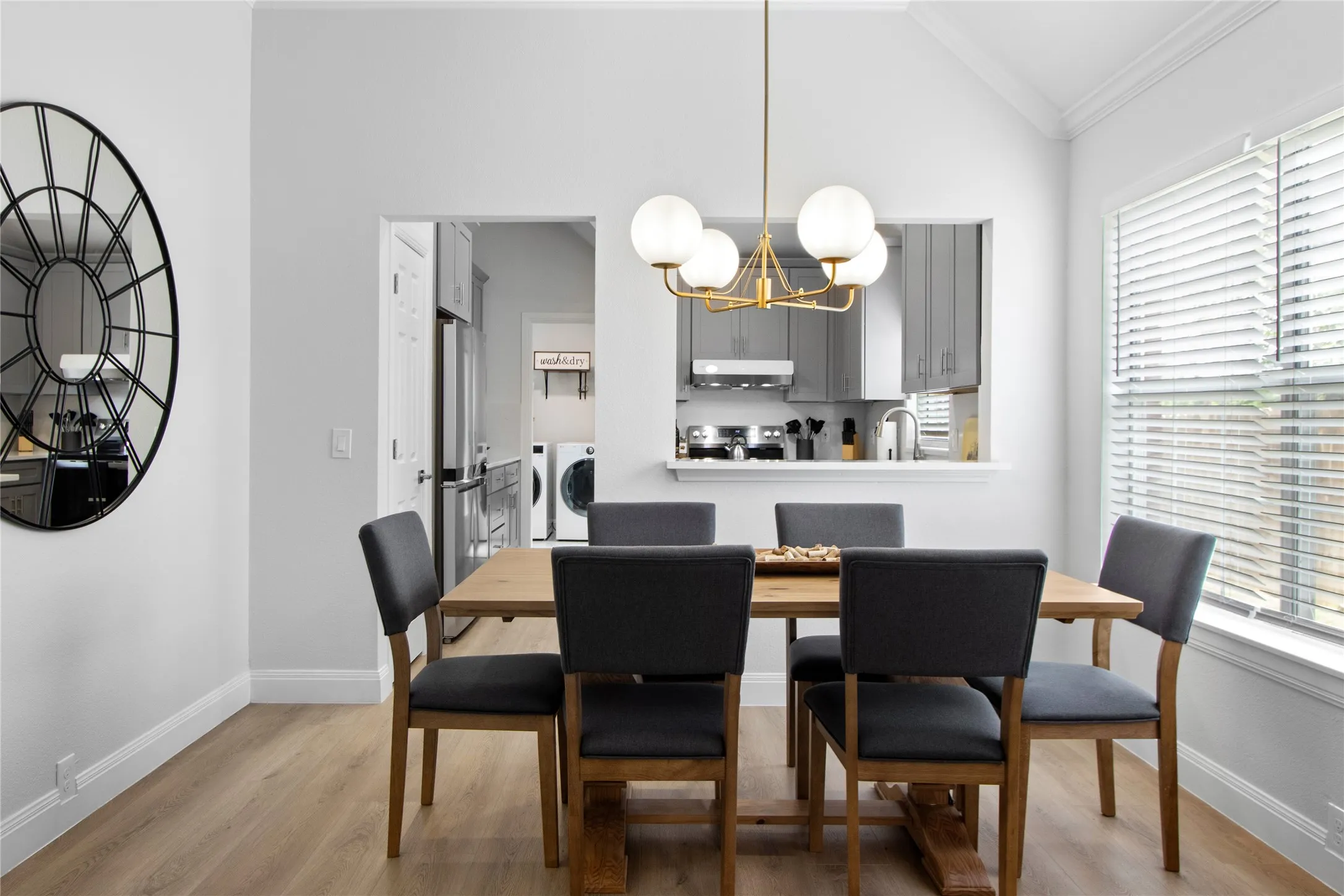 Dining area featuring wood-finish flooring, a contemporary chandelier, and a large window with horizontal blinds